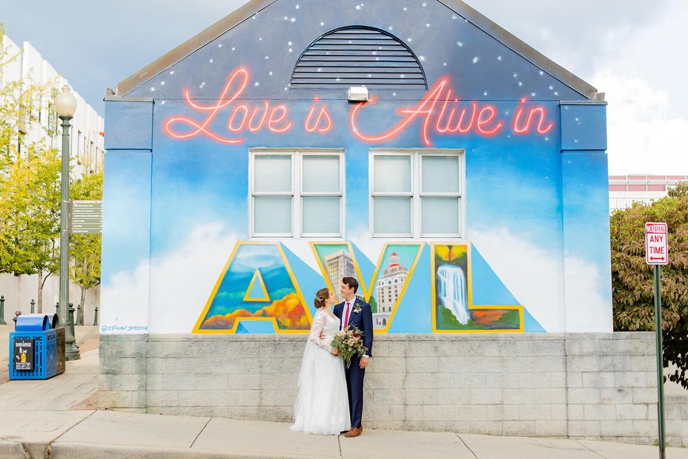 bride and groom in front of the spicer greene jewelers Love is Alive in AVL graffiti wall