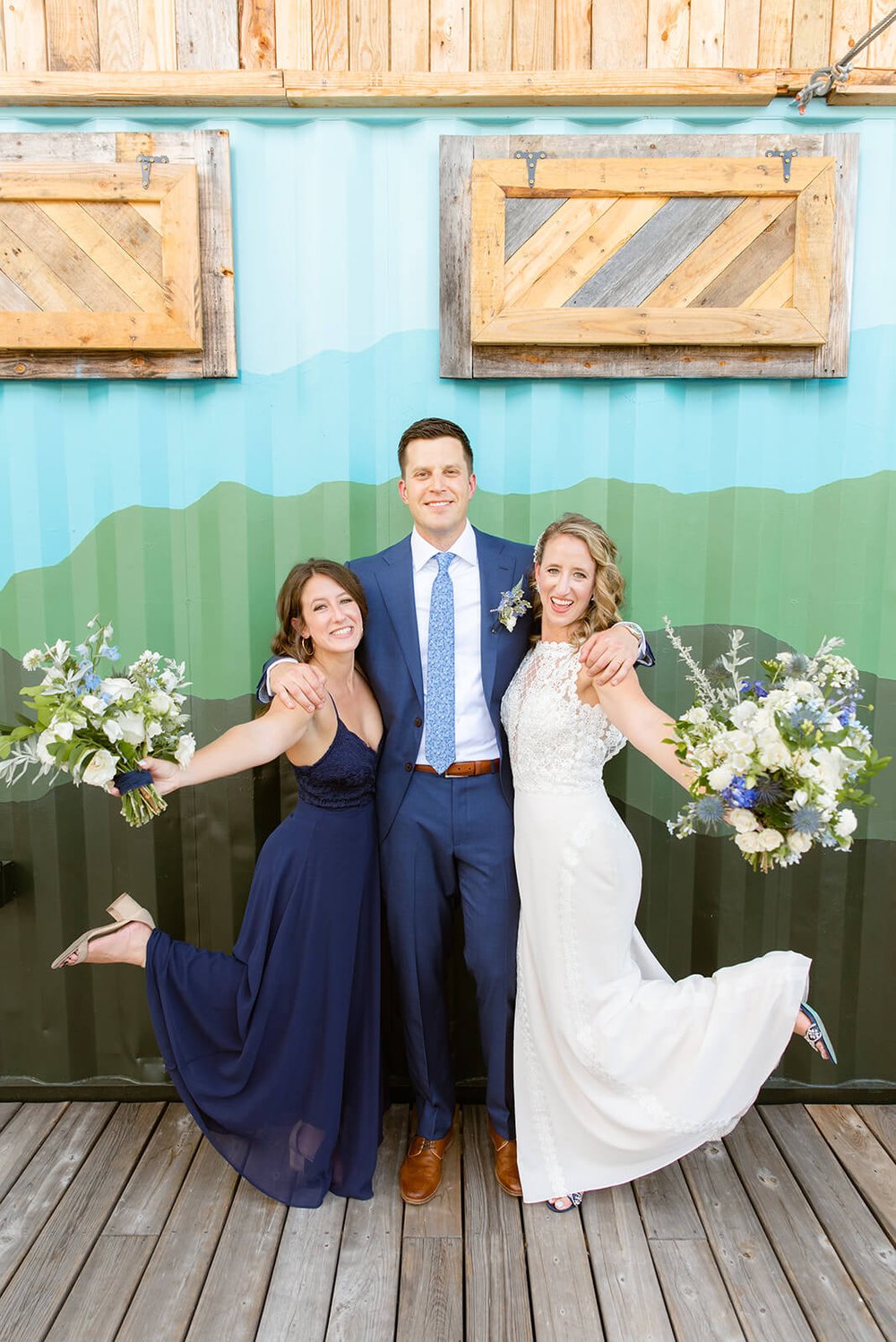 bride, groom, and maid of honor in front of colorful wall at highland brewing