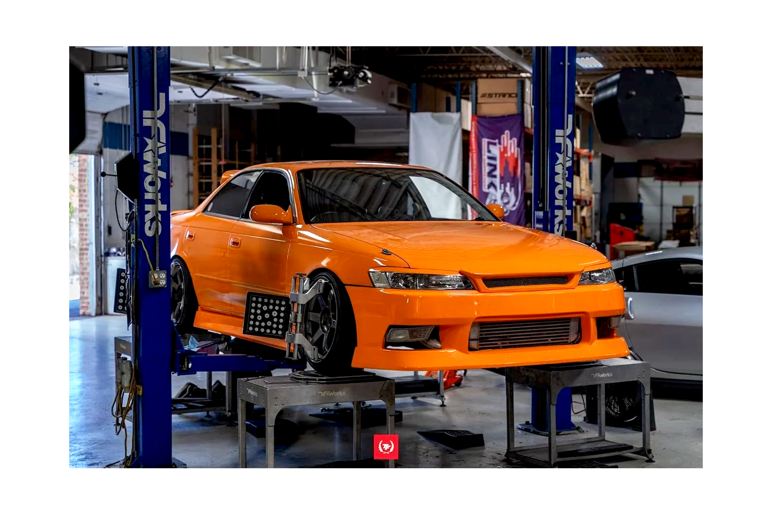 Orange race car on hydraulic lift in garage.