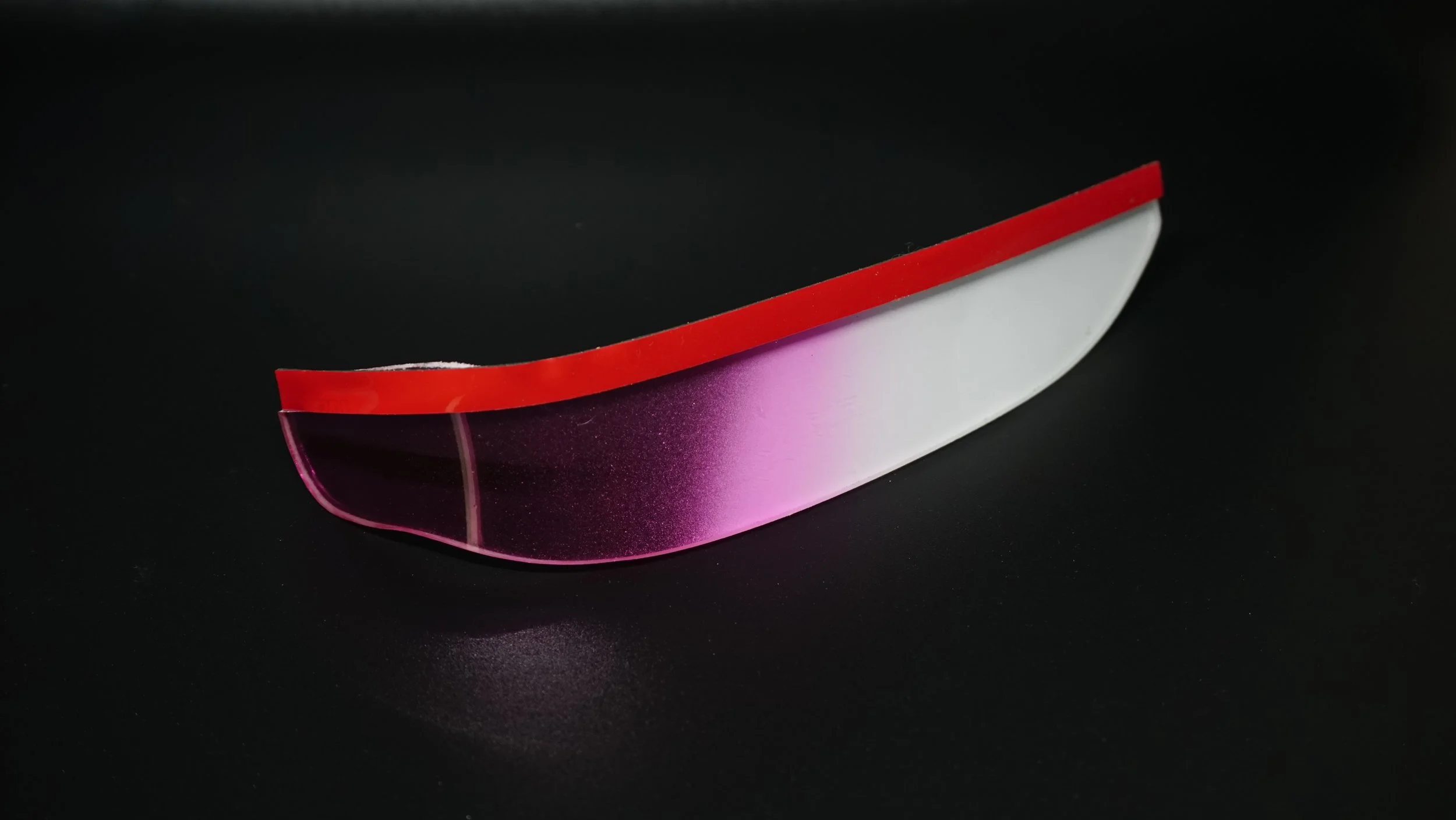 A rectangular object with a pink translucent bottom and a red top edge, set against a black background.