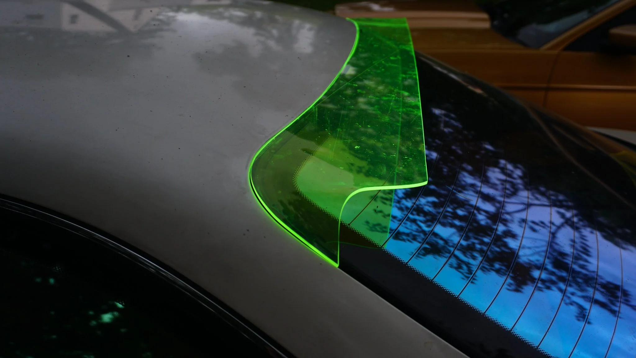 Green laser or reflective decal on the rear window of a black car, with trees reflecting on the glass.