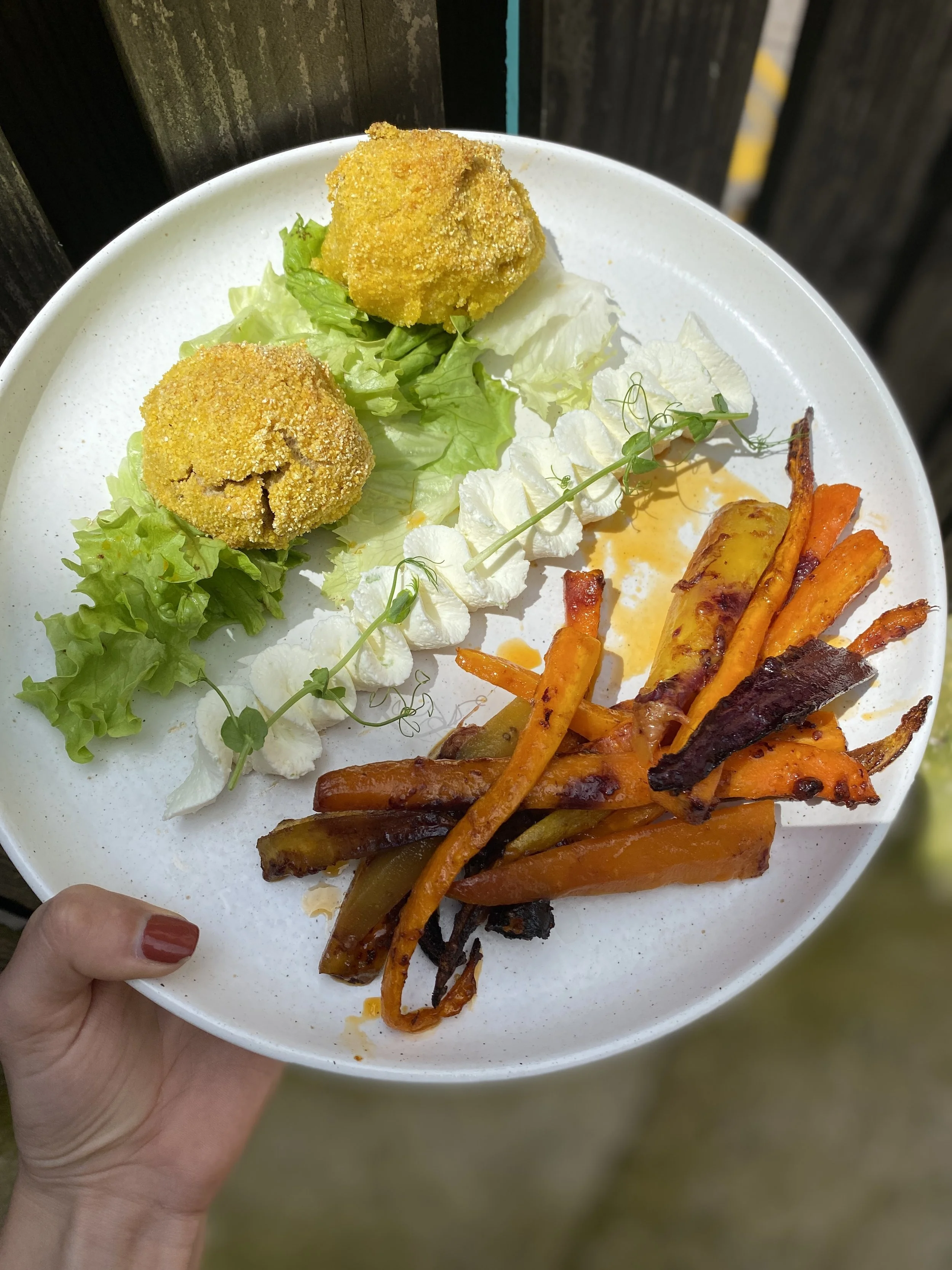 Assiette blanche avec deux croquettes, salade verte, crème, pousses, et légumes grillés ou rôtis.