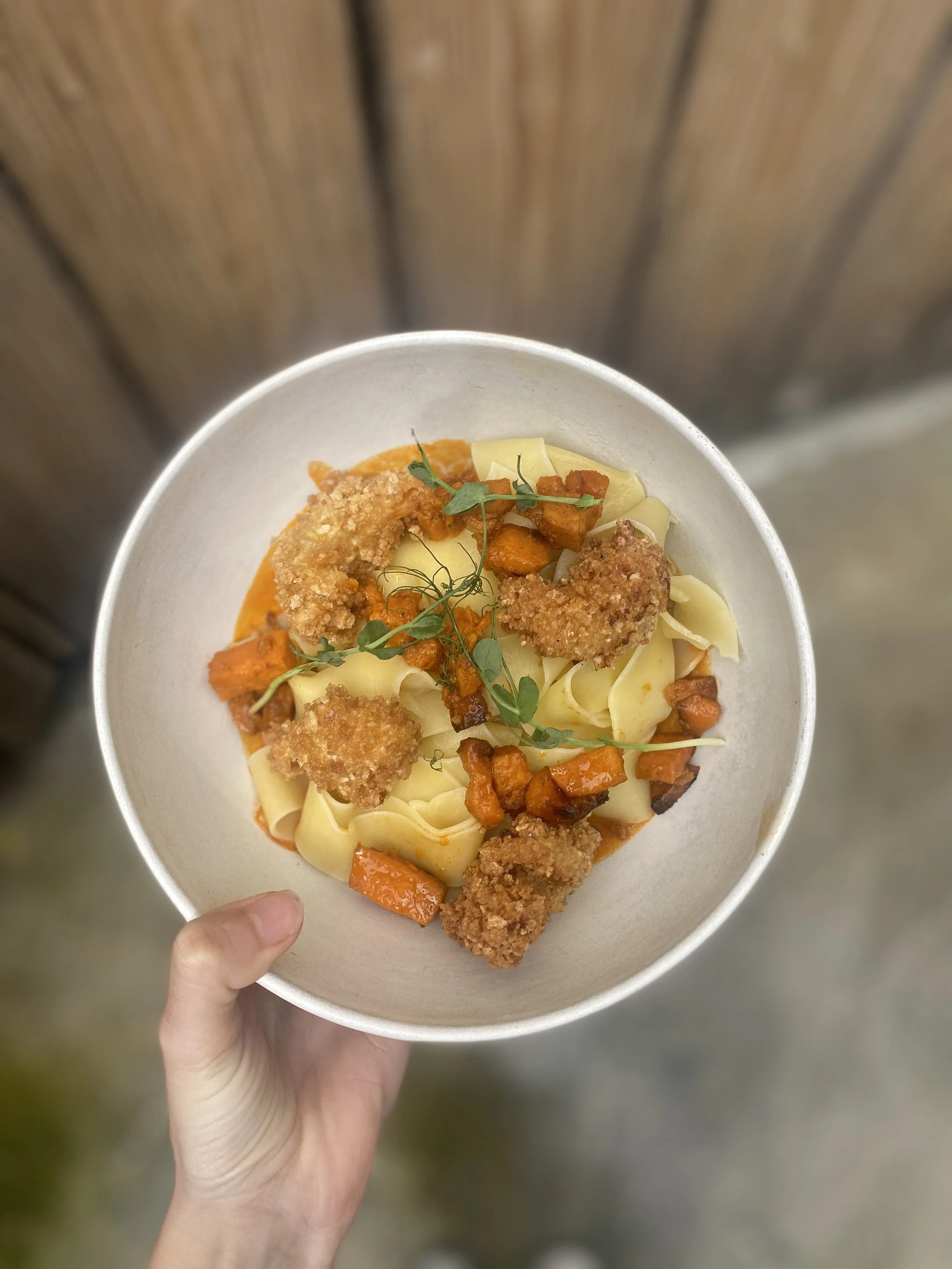 Bol de pâtes avec morceaux de carottes, croquettes de poulet, garniture verte, dans un bol en papier