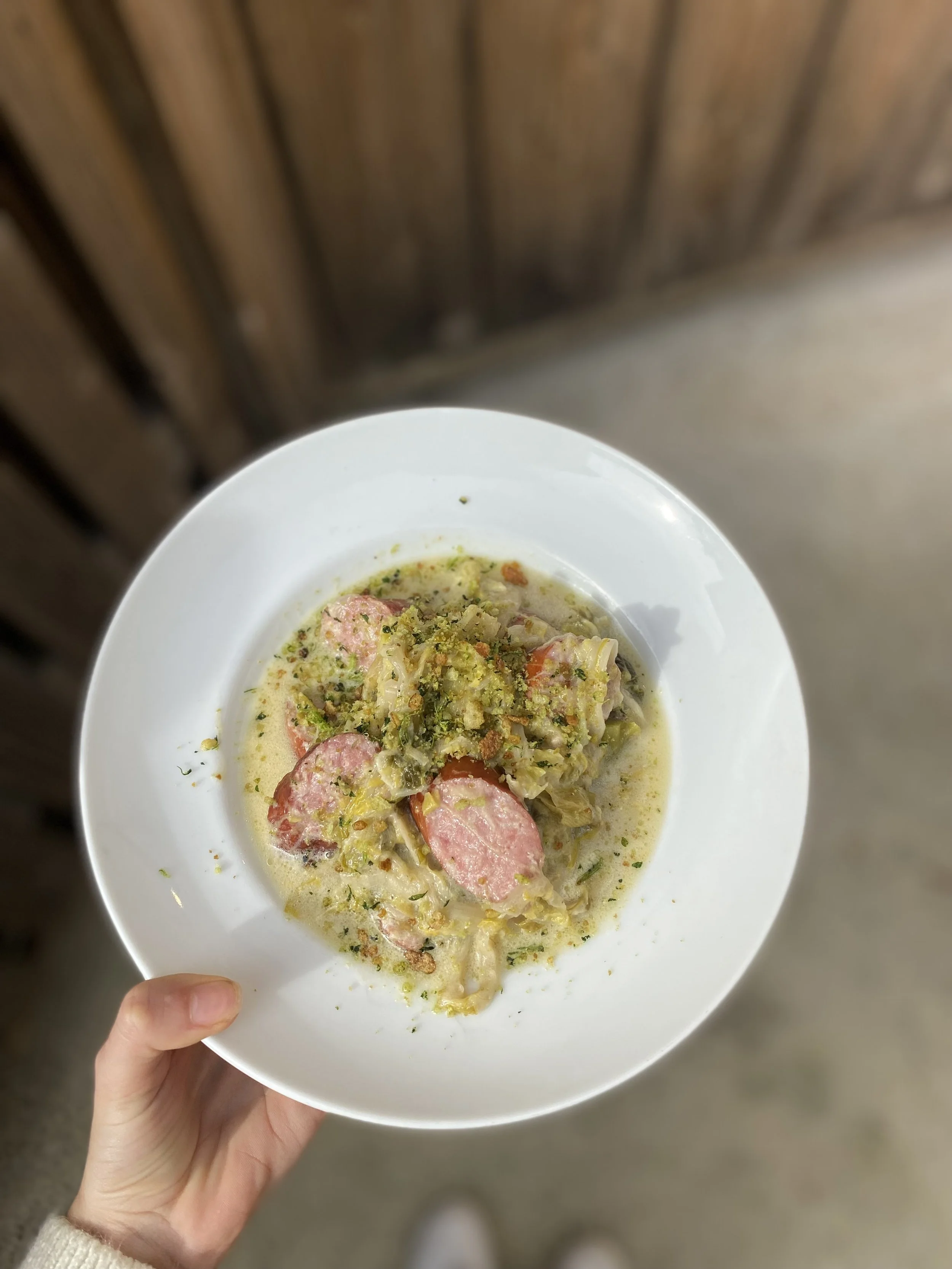 Assiette de repas contenant des saucisses, légumes, et une sauce crémeuse, vue du dessus.