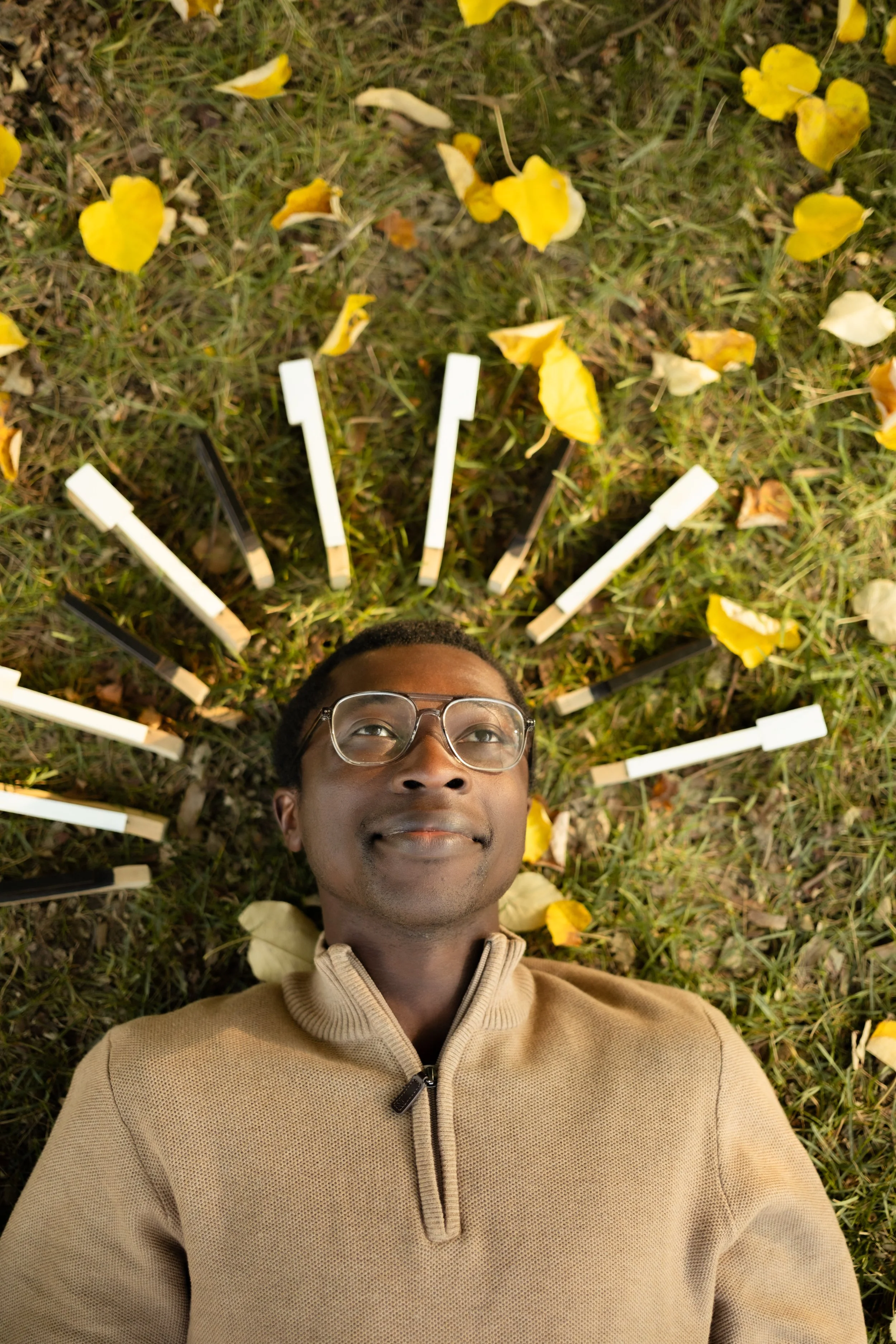 Person lying on grass surrounded by yellow flower petals, taking a selfie.