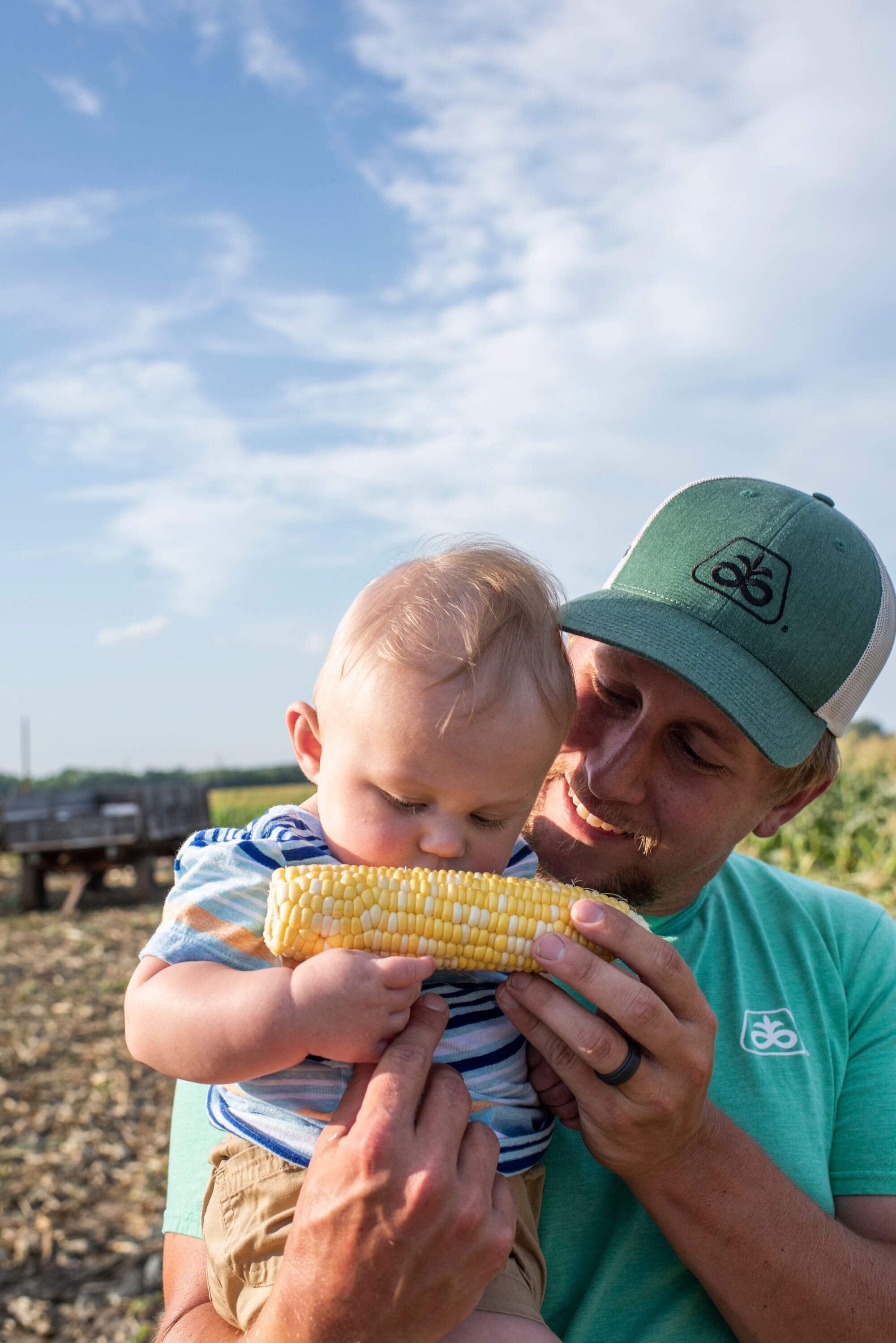 A cute baby eating sweet corn with his dad