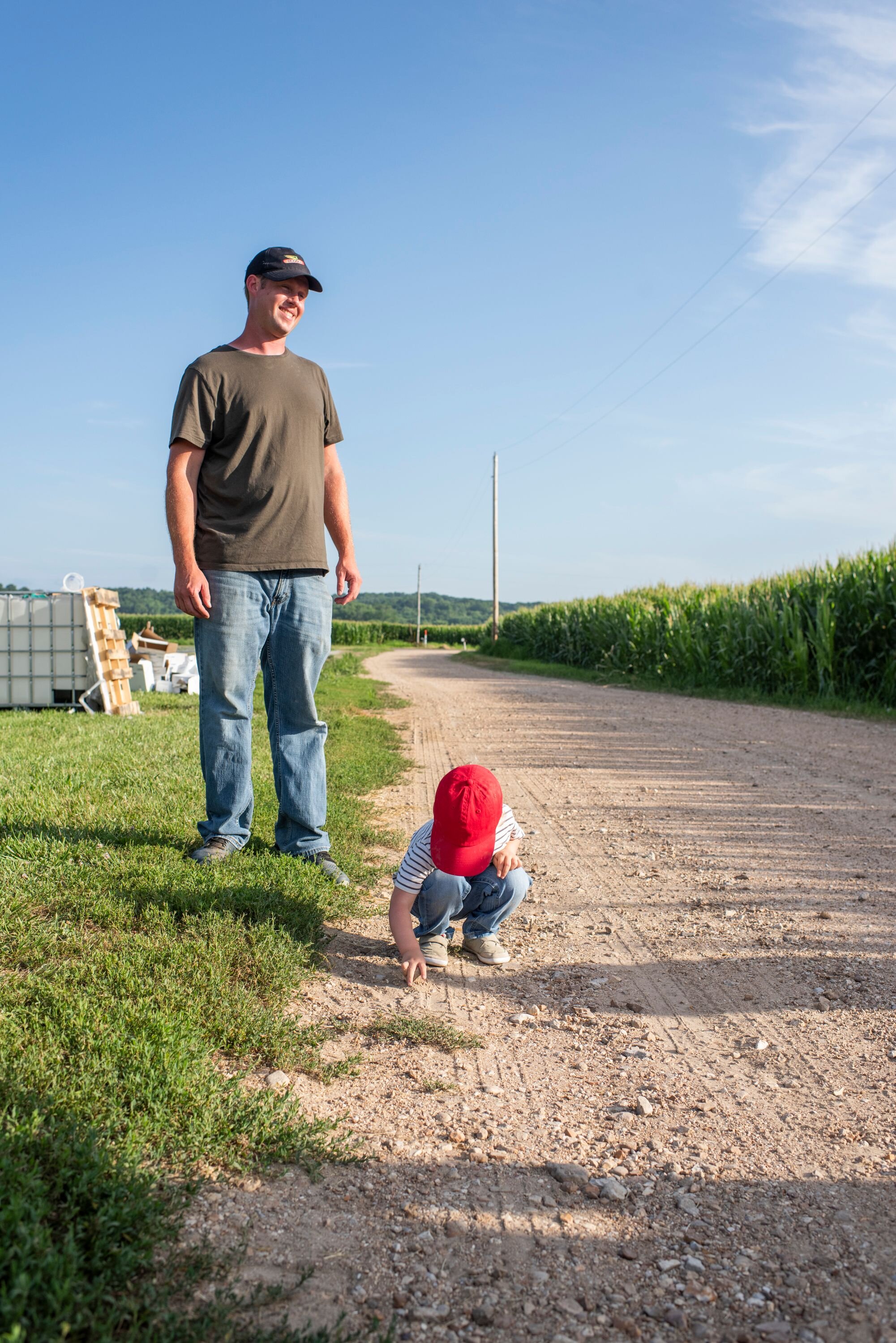 A father looks on as his young child plays in the dirt at their family farm