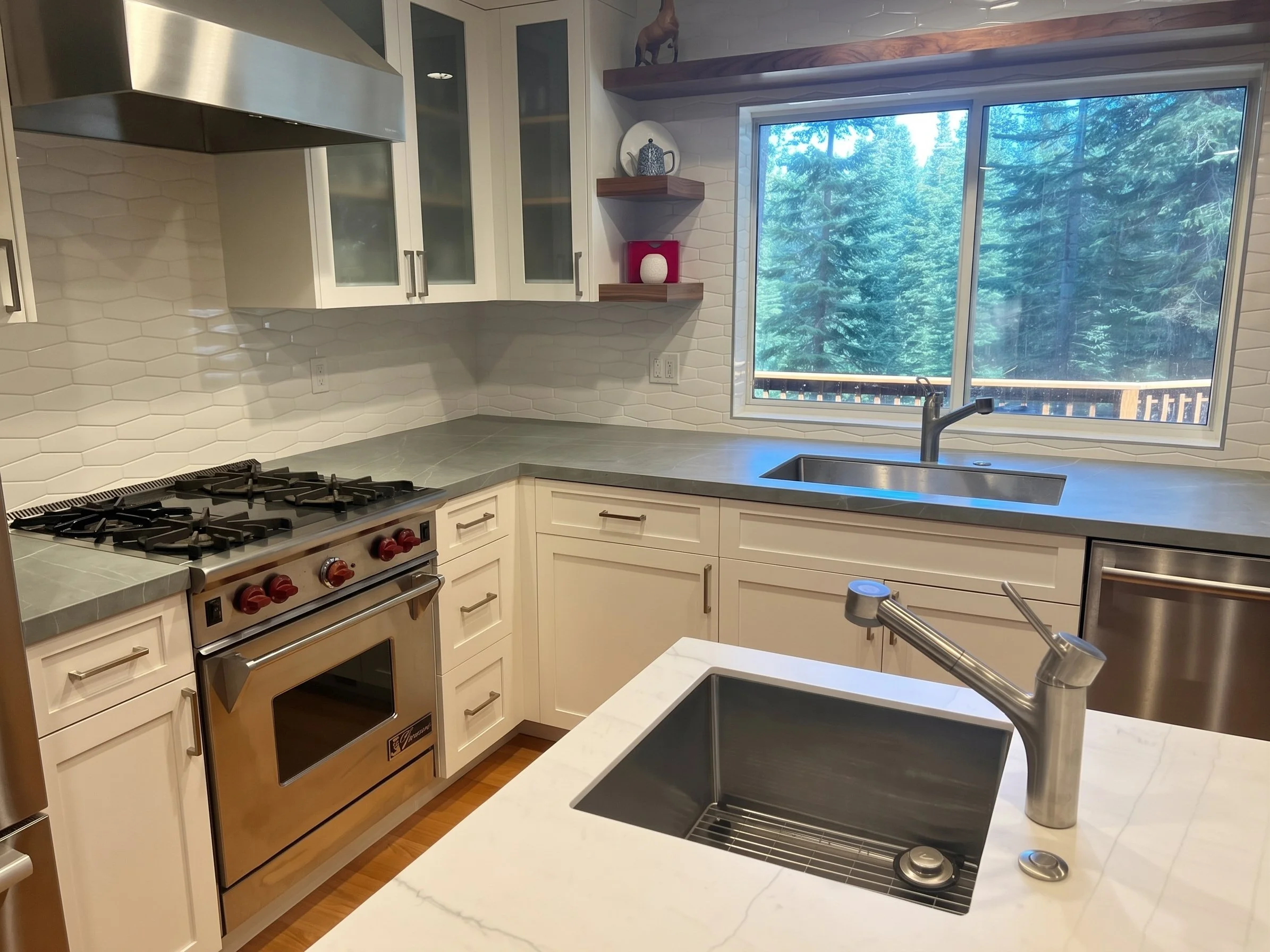 Range, sink and window over gray stone counters, seen across the island sink.