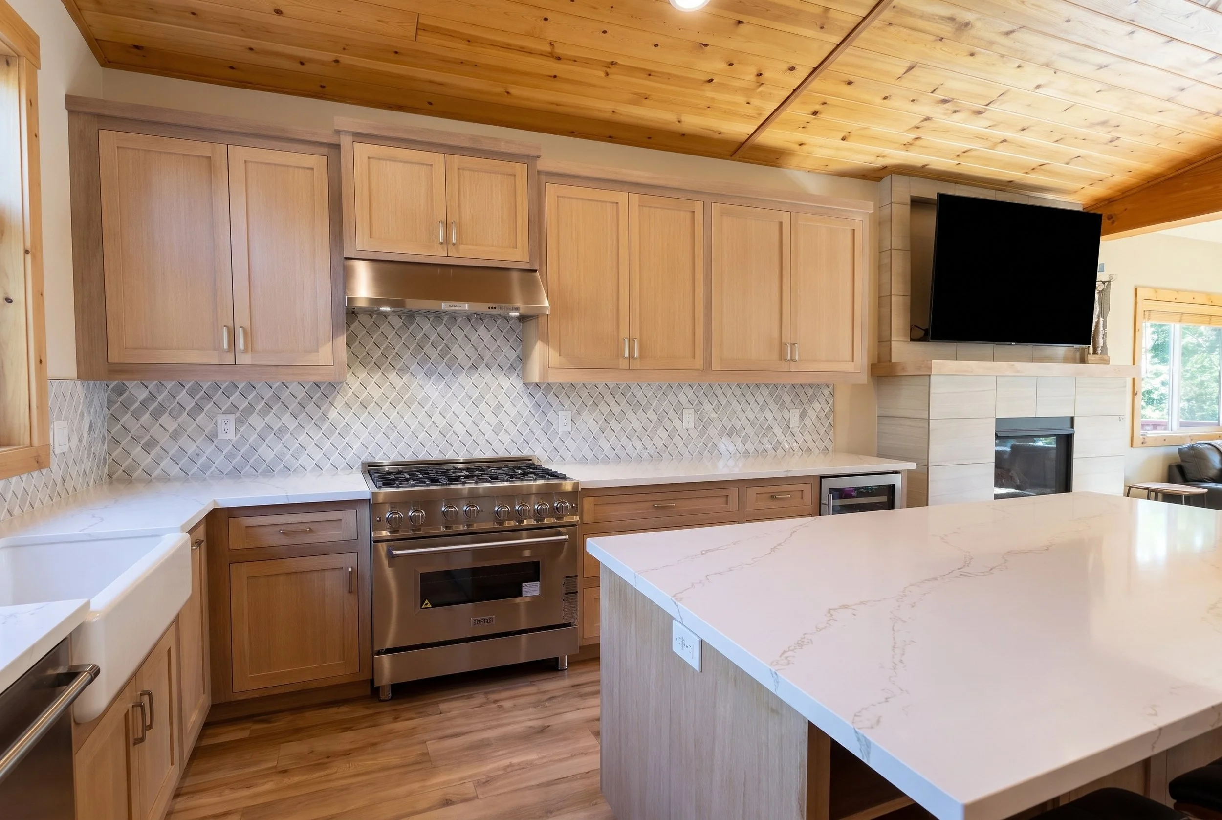 Kitchen with natural wood shaker cabinets, a white quartz island and a wood plank ceiling.
