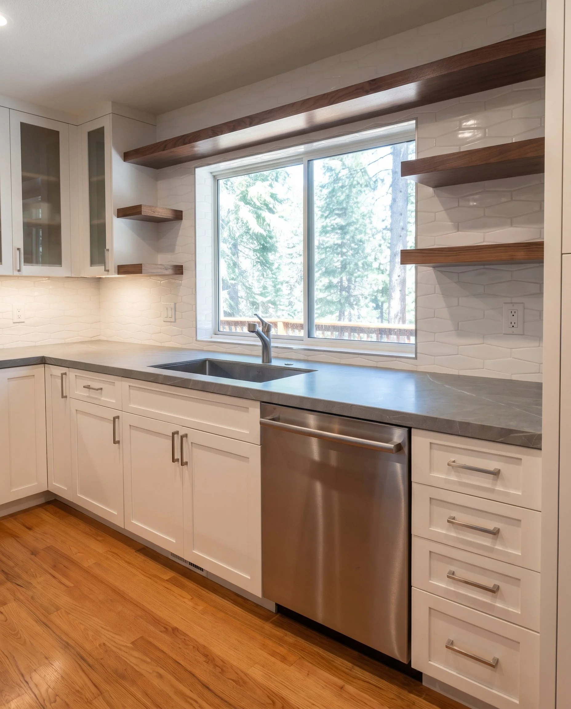 Sink run with gray stone counters, a stainless dishwasher and a window over the sink.