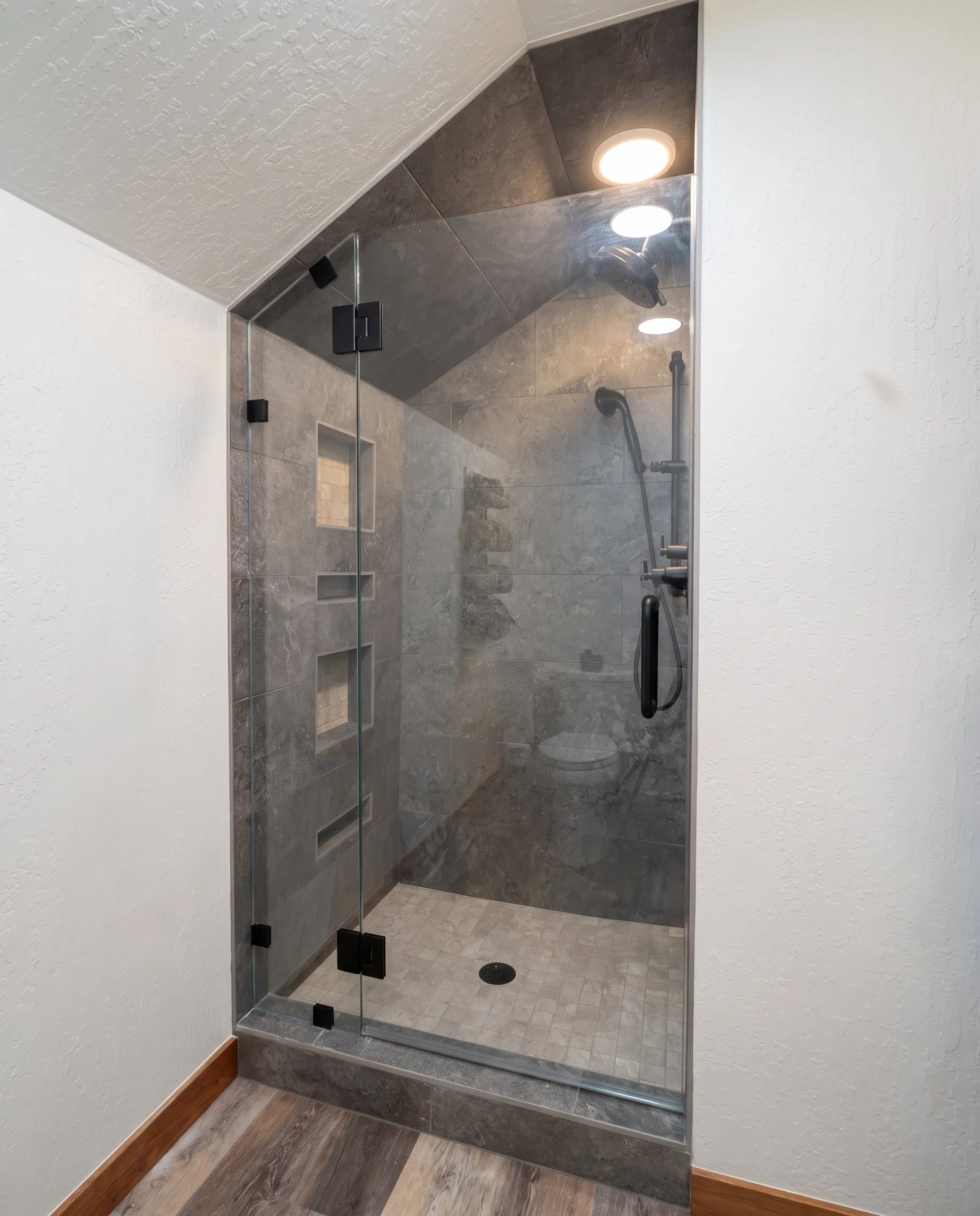 Tiled shower with a glass door, seen from the bath.