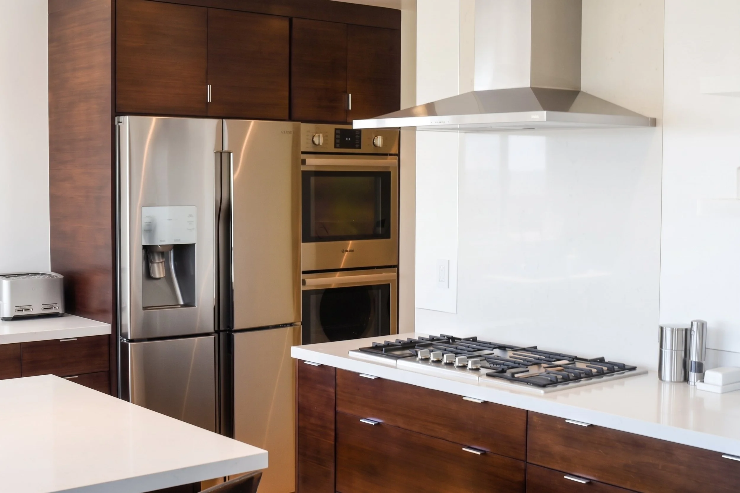 Cooktop, wall ovens and refrigerator set in dark wood cabinets.