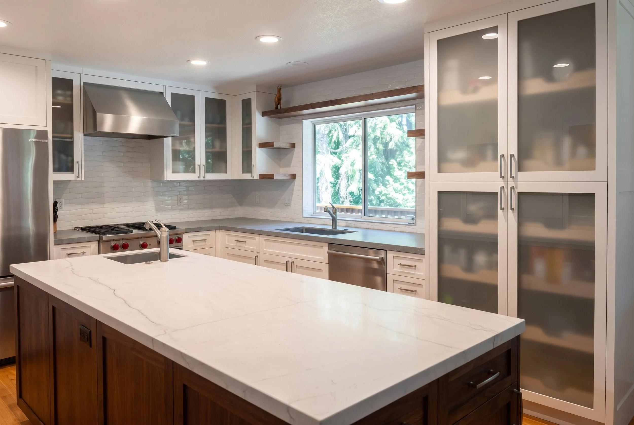 Wide view across the white stone island to the sink wall and frosted glass cabinets.