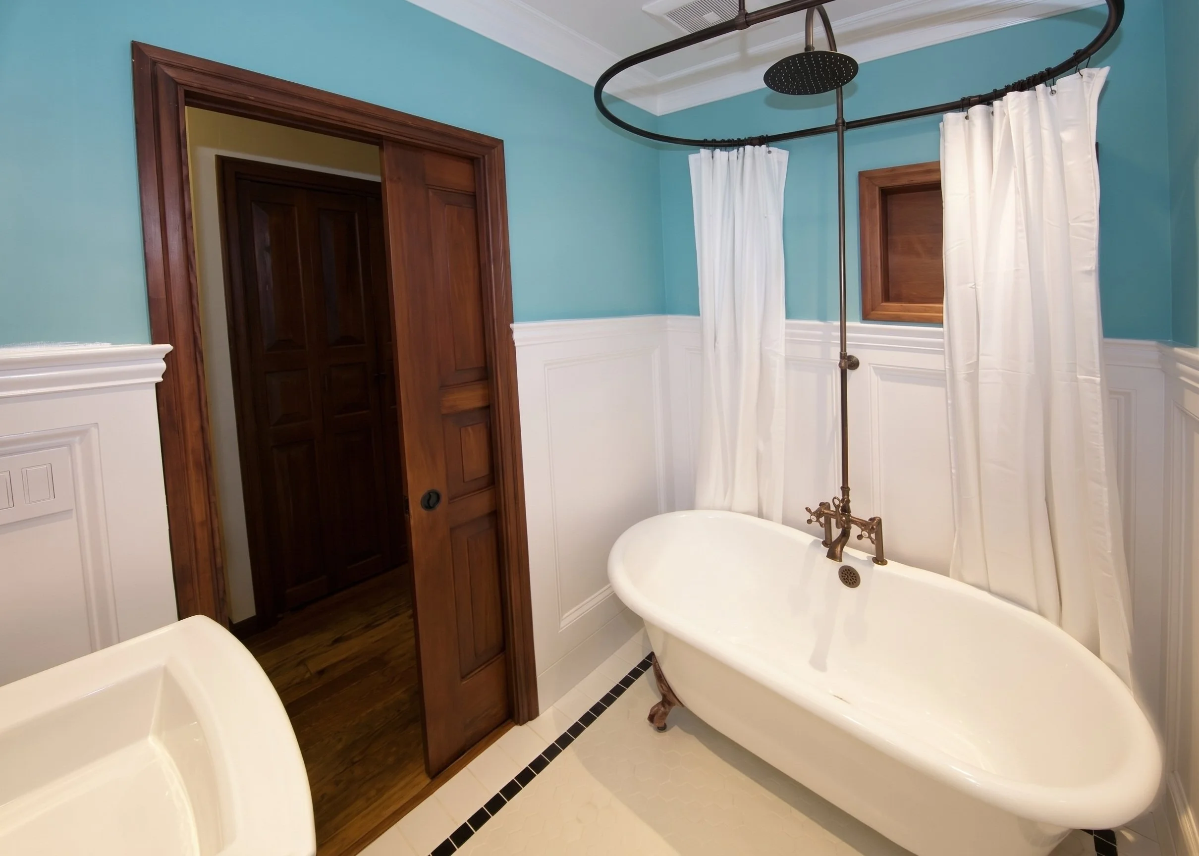 Period bathroom with a clawfoot tub, paneled wainscot and a ring shower curtain rod.