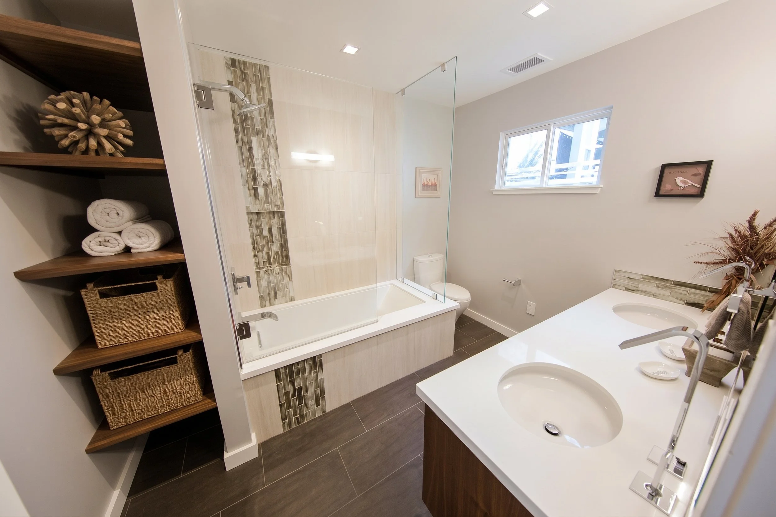 Bathroom with a tub and shower behind a glass panel, a double vanity and built-in wood shelves.
