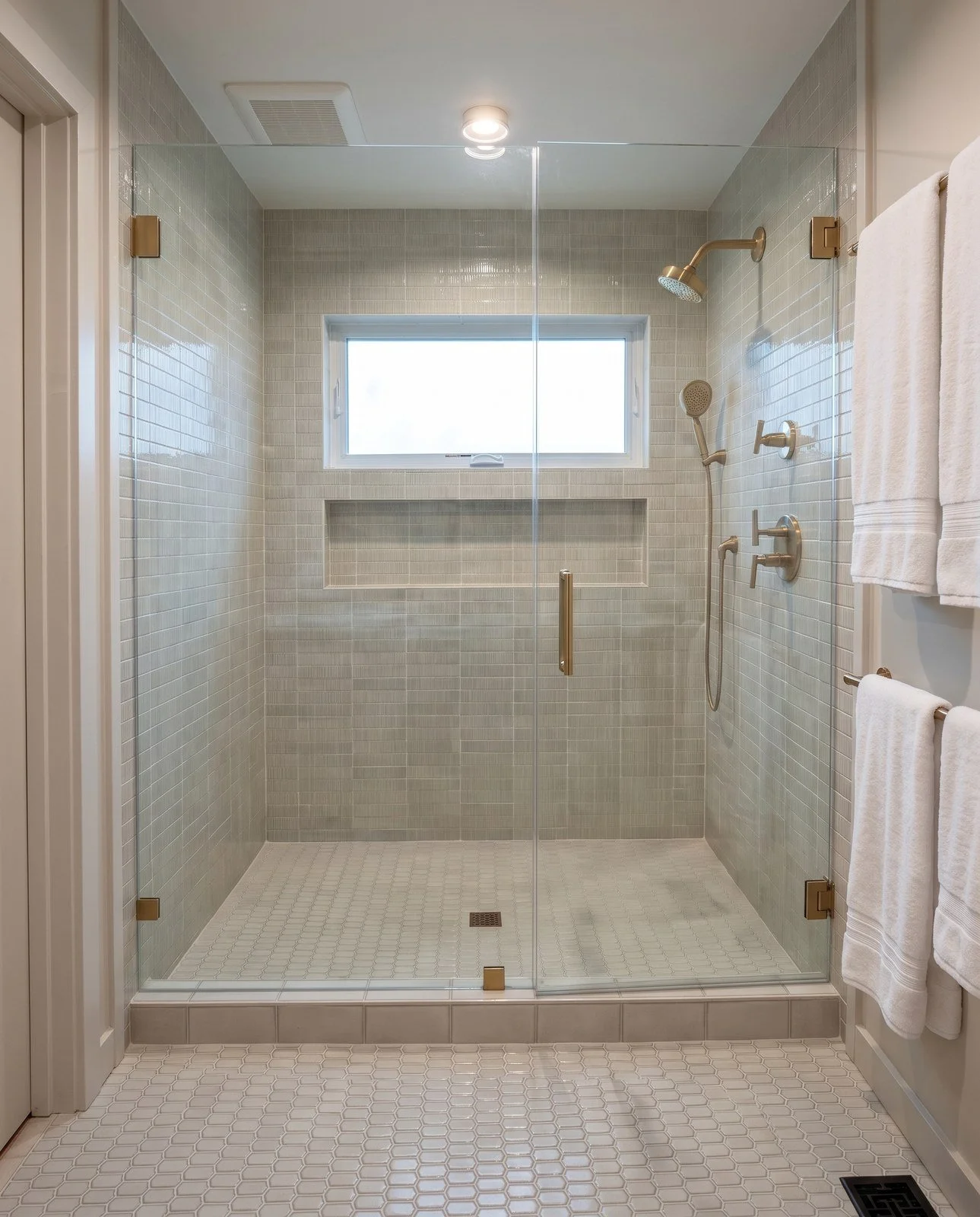 Walk-in shower with glazed tile walls, a long recessed niche, a frameless glass door and brass shower fittings.