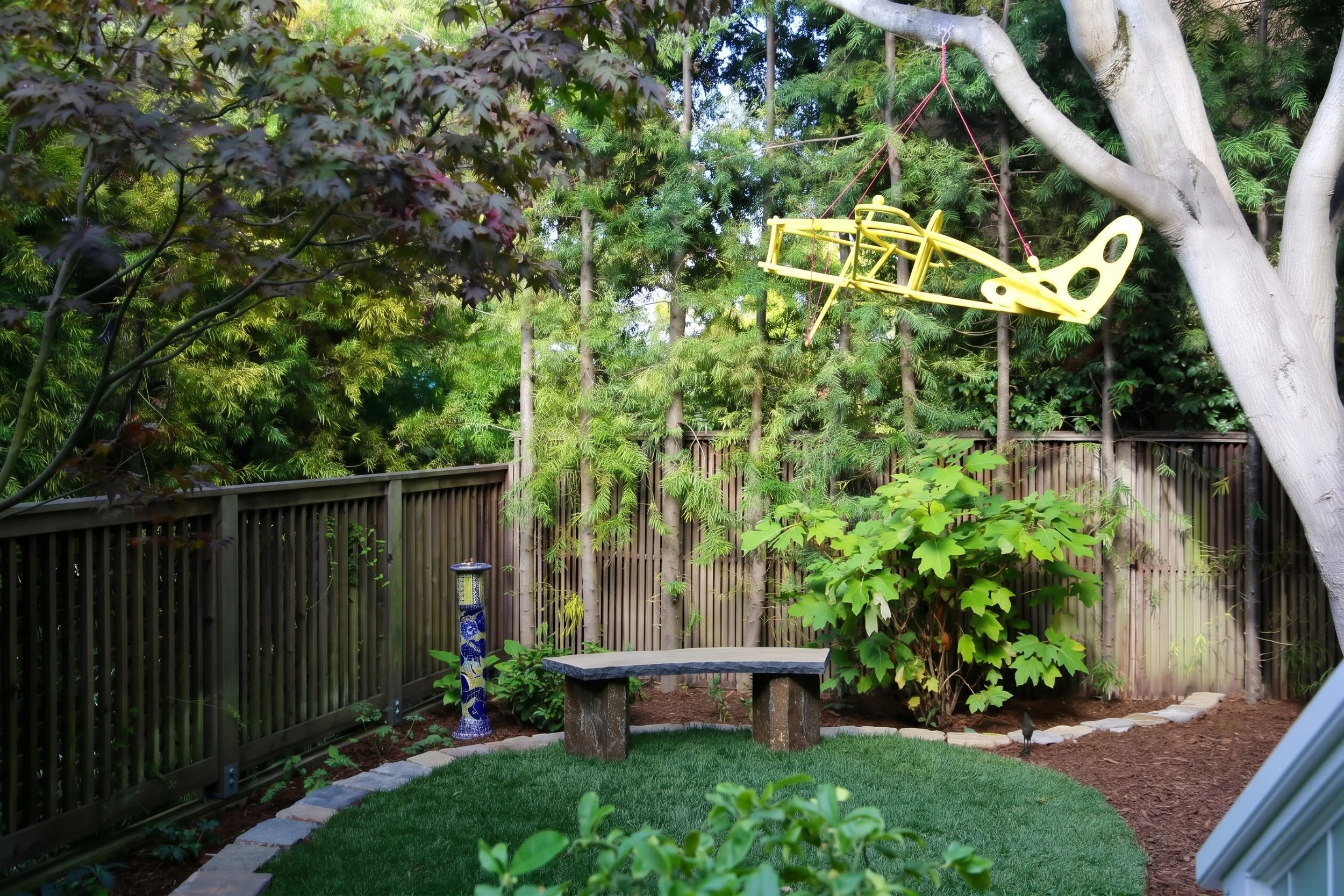 Garden with a bench under a tree and a sculpture.