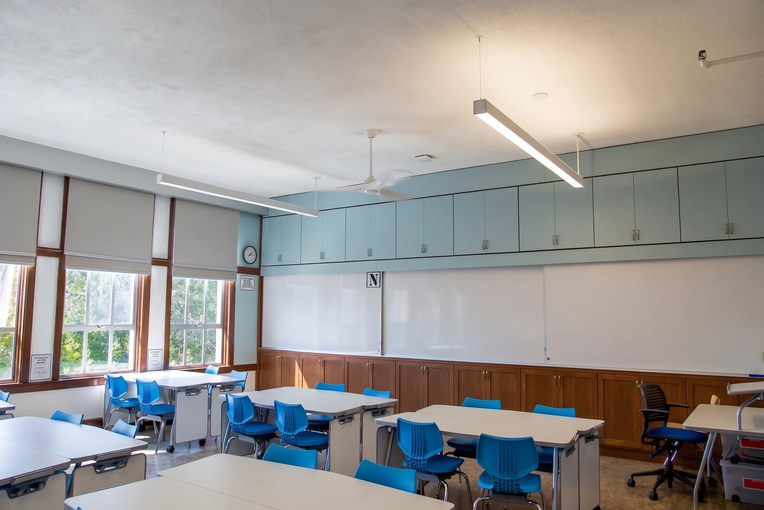 Classroom wall of cabinets and whiteboards with desks in front.