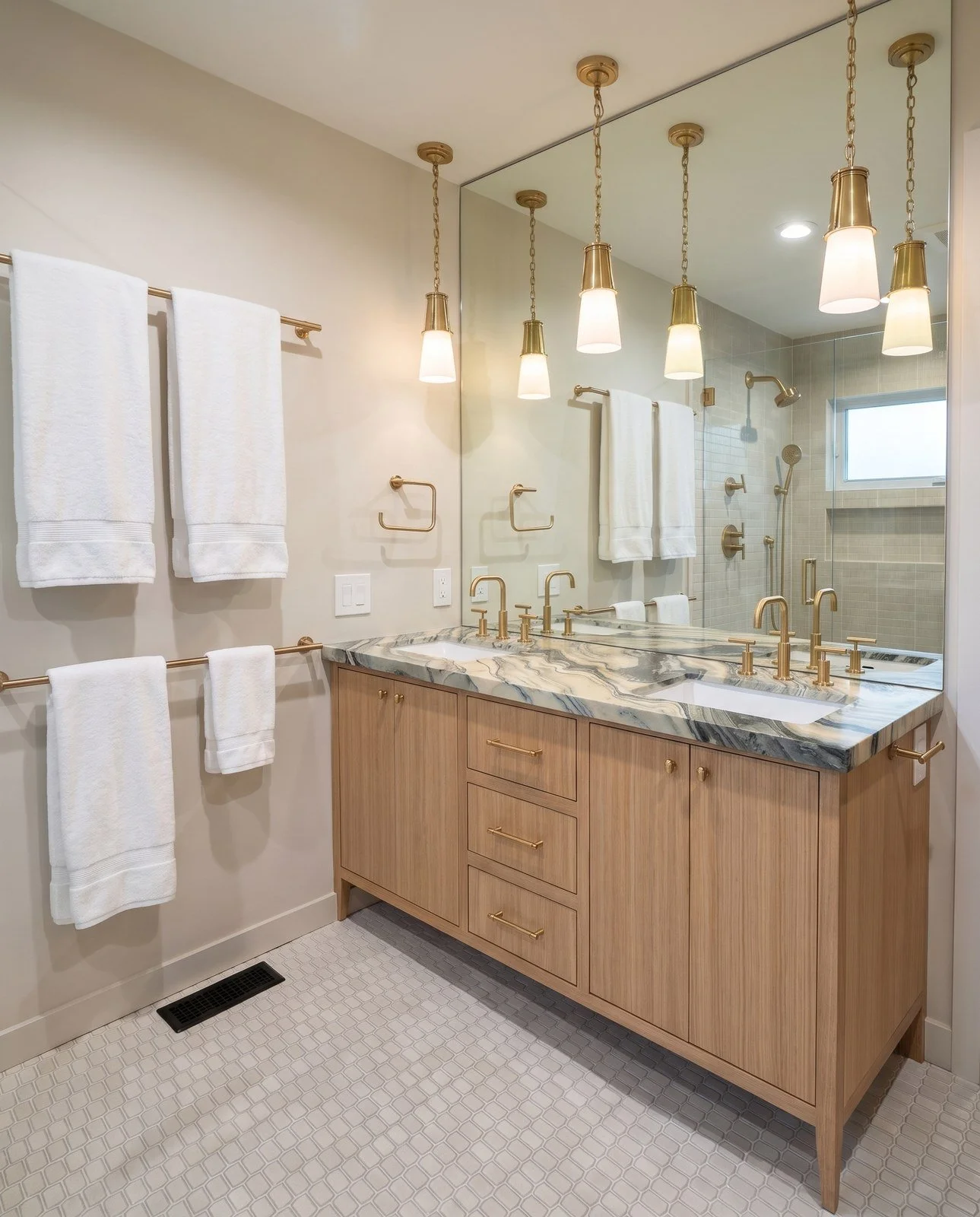 Oak double vanity with a veined stone top, two sinks, brass faucets and three brass pendant lights in front of a large mirror.