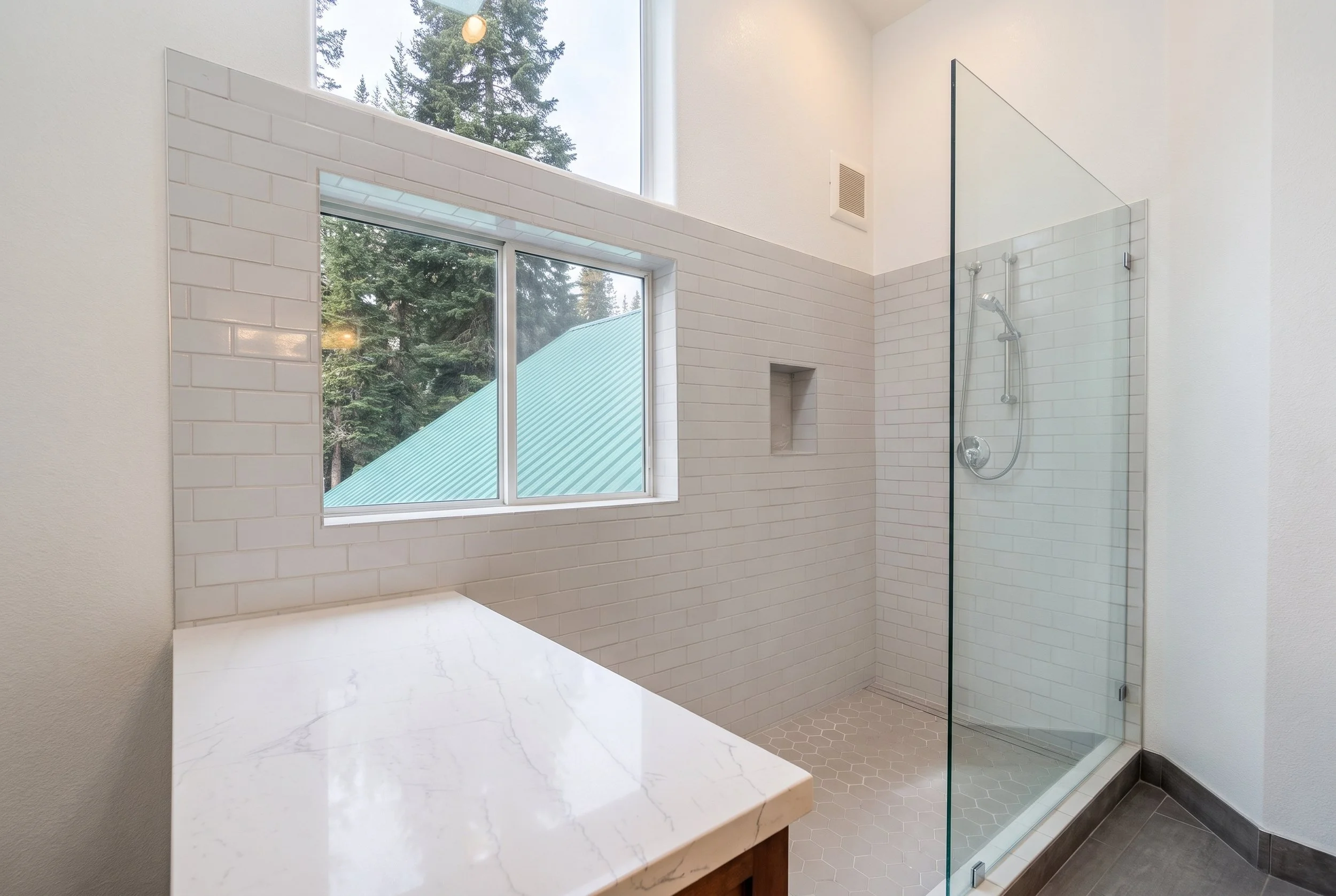 Stone-topped shower bench under the window, with white subway tile and a glass panel.