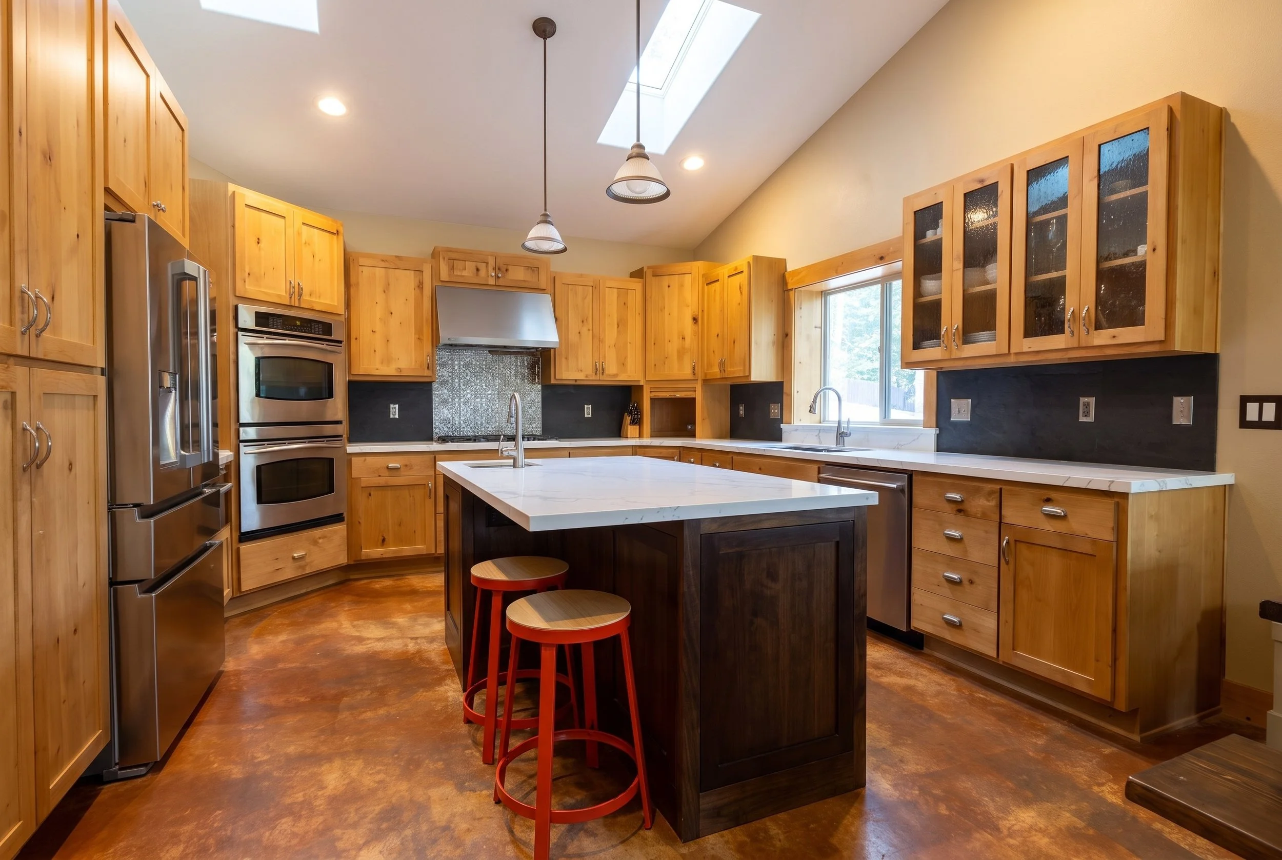 Kitchen with knotty alder cabinets, glass-front uppers, a dark wood island with a quartz top and a stained concrete floor.
