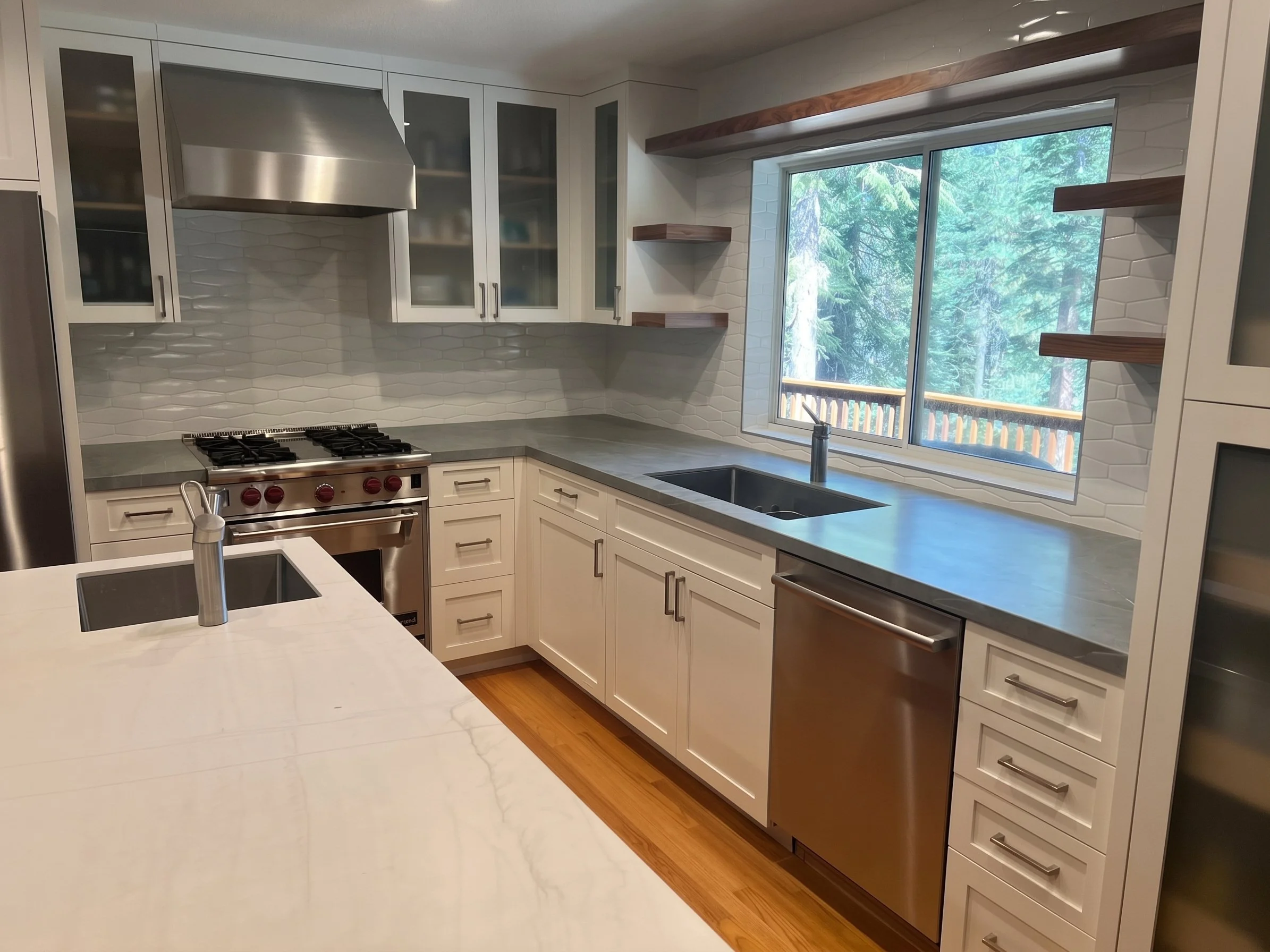 Sink wall with the range, dishwasher and wood floating shelves, seen from the island.