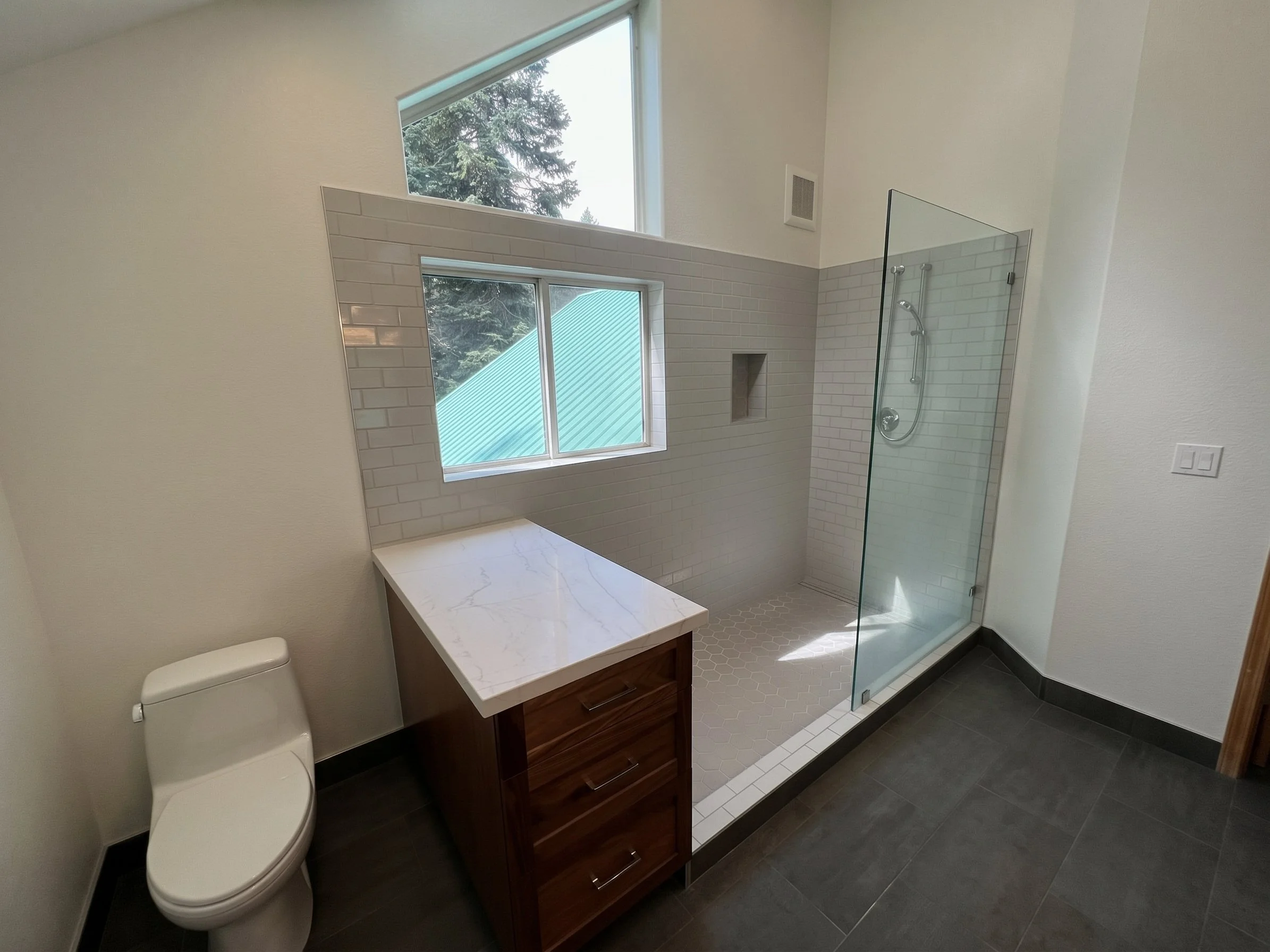 Walk-in shower with a glass panel, white subway tile and a stone-topped bench, beside a dark wood vanity.