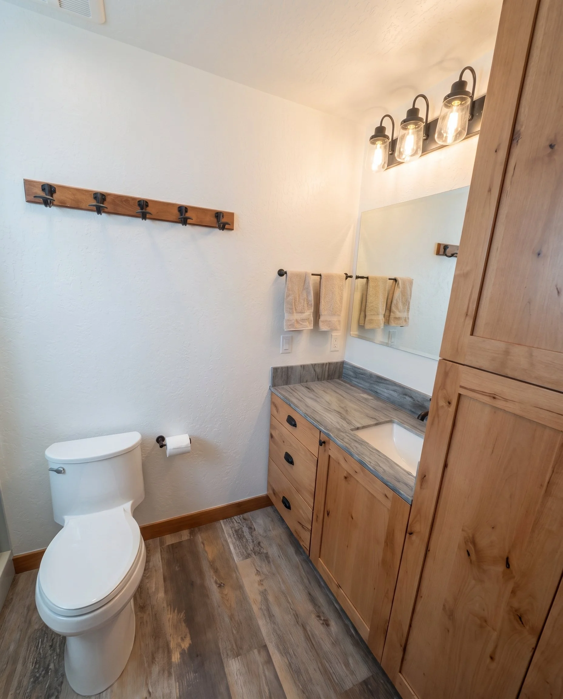 Bath vanity with a stone top beside a knotty alder linen cabinet.