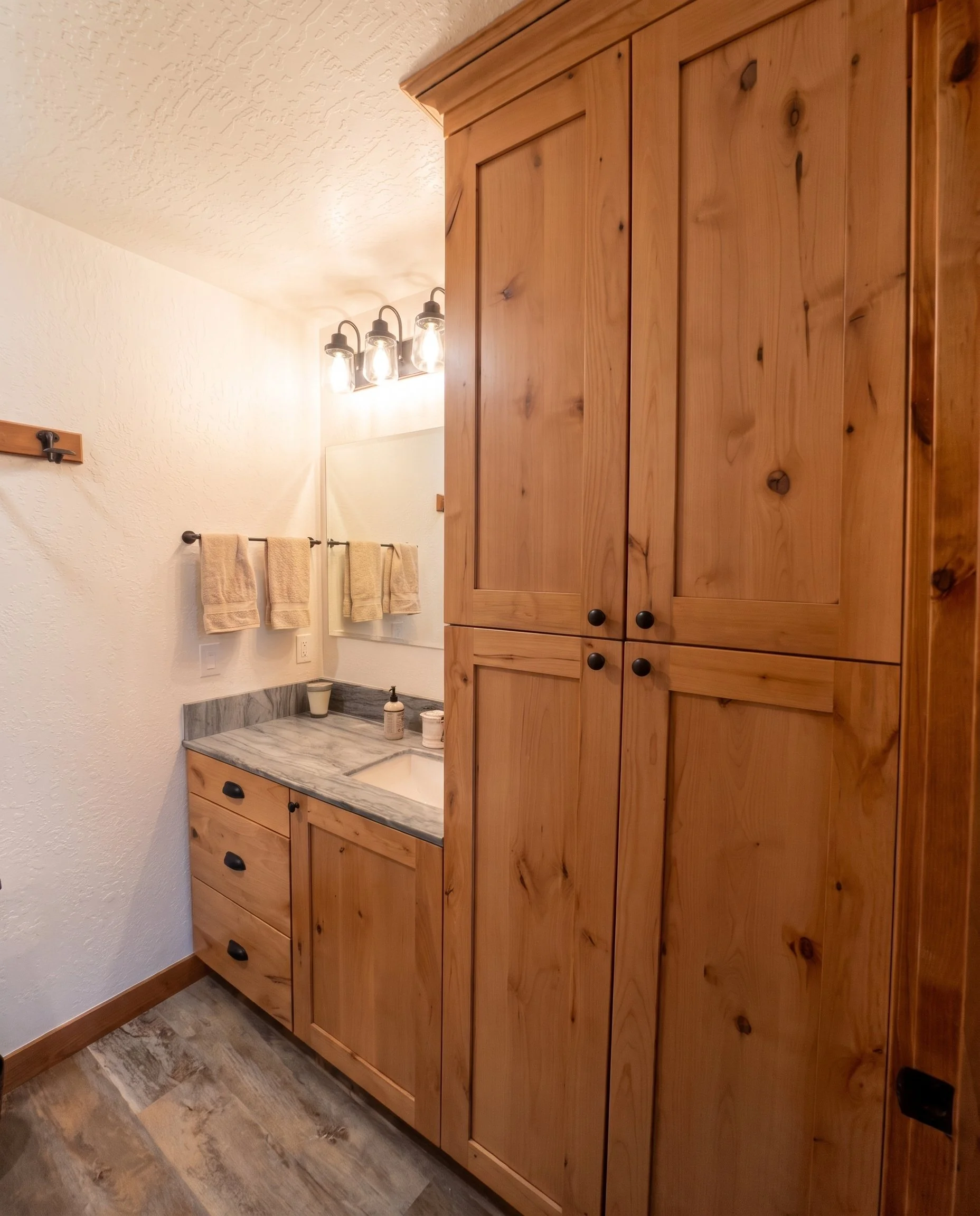 Tall knotty alder linen cabinet beside the bath vanity.