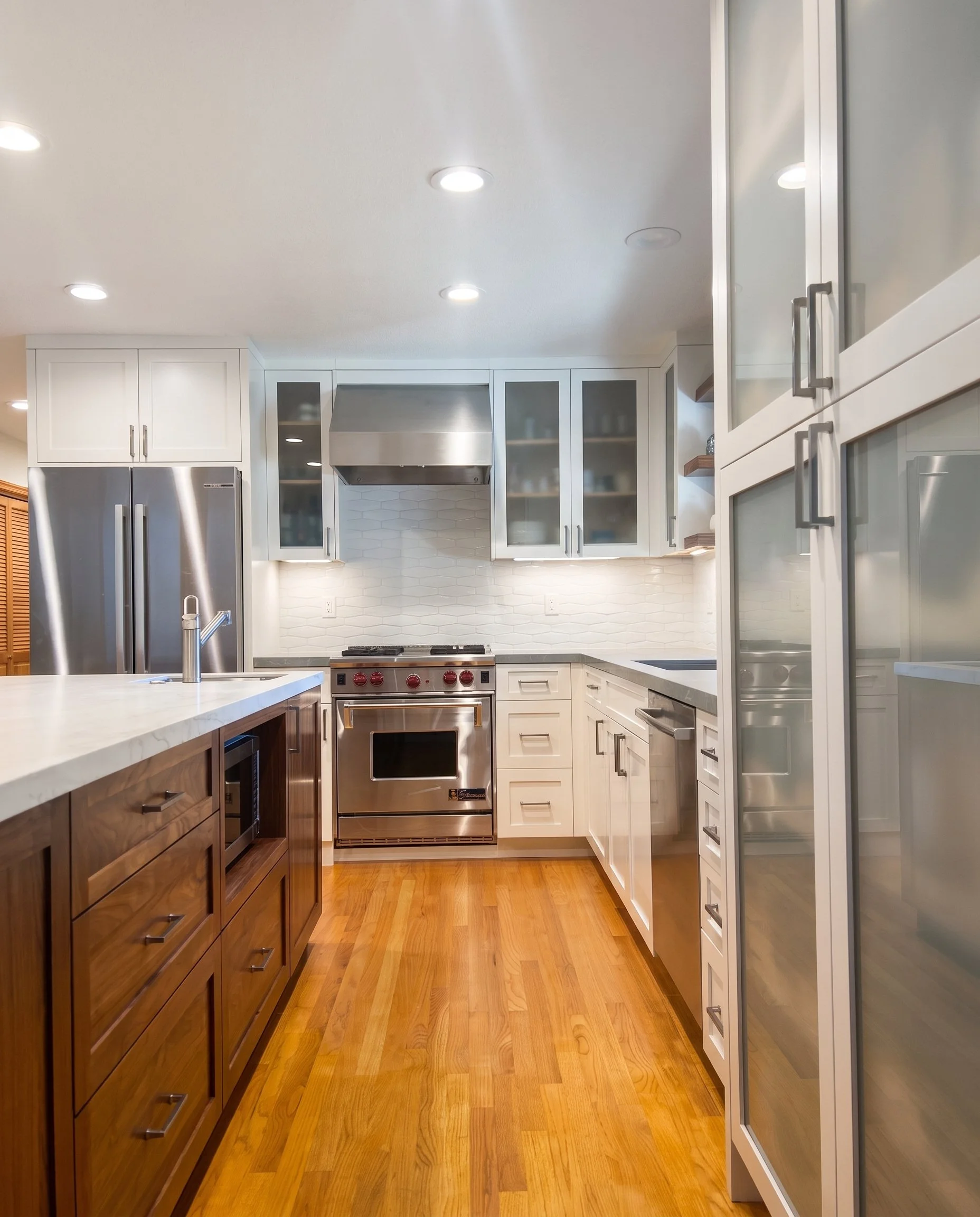 View down the kitchen between the island and the tall glass cabinets toward the range.