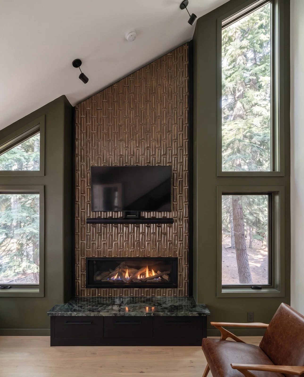 Full-height dark glazed tile fireplace wall with a wall-mounted TV, linear gas fireplace and stone hearth, between tall windows.
