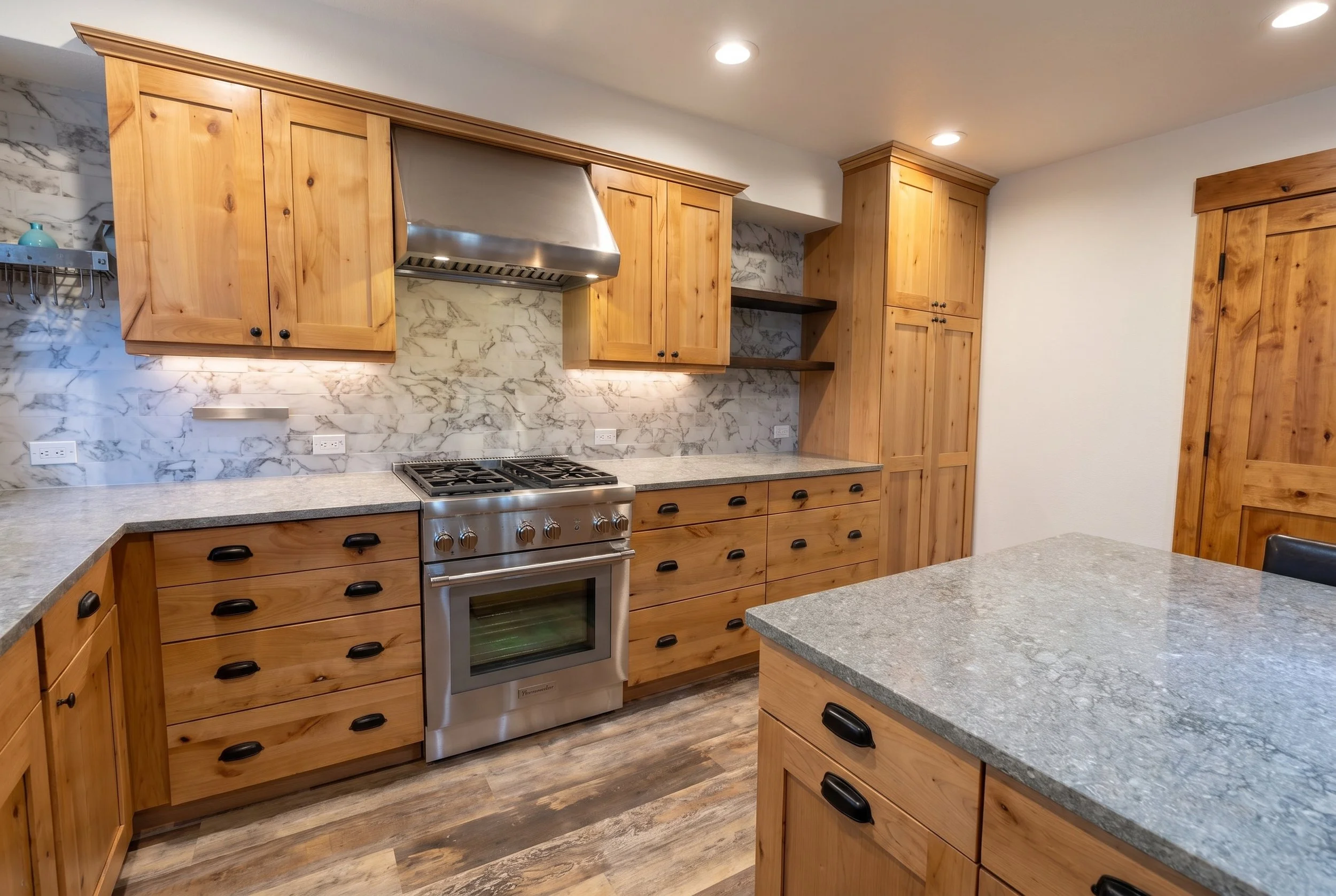 Range and island corner with knotty alder cabinets, black hardware and stone counters.