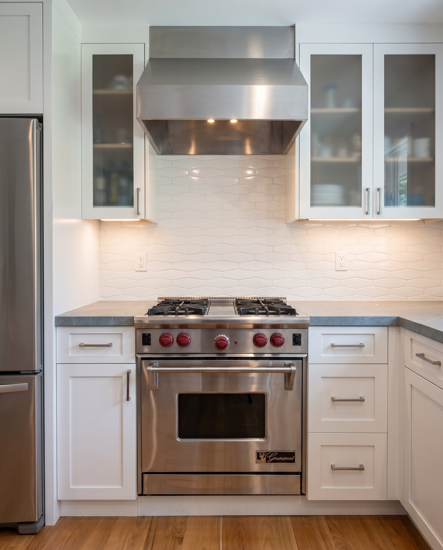 Range and stainless hood seen straight on, between glass-front upper cabinets.