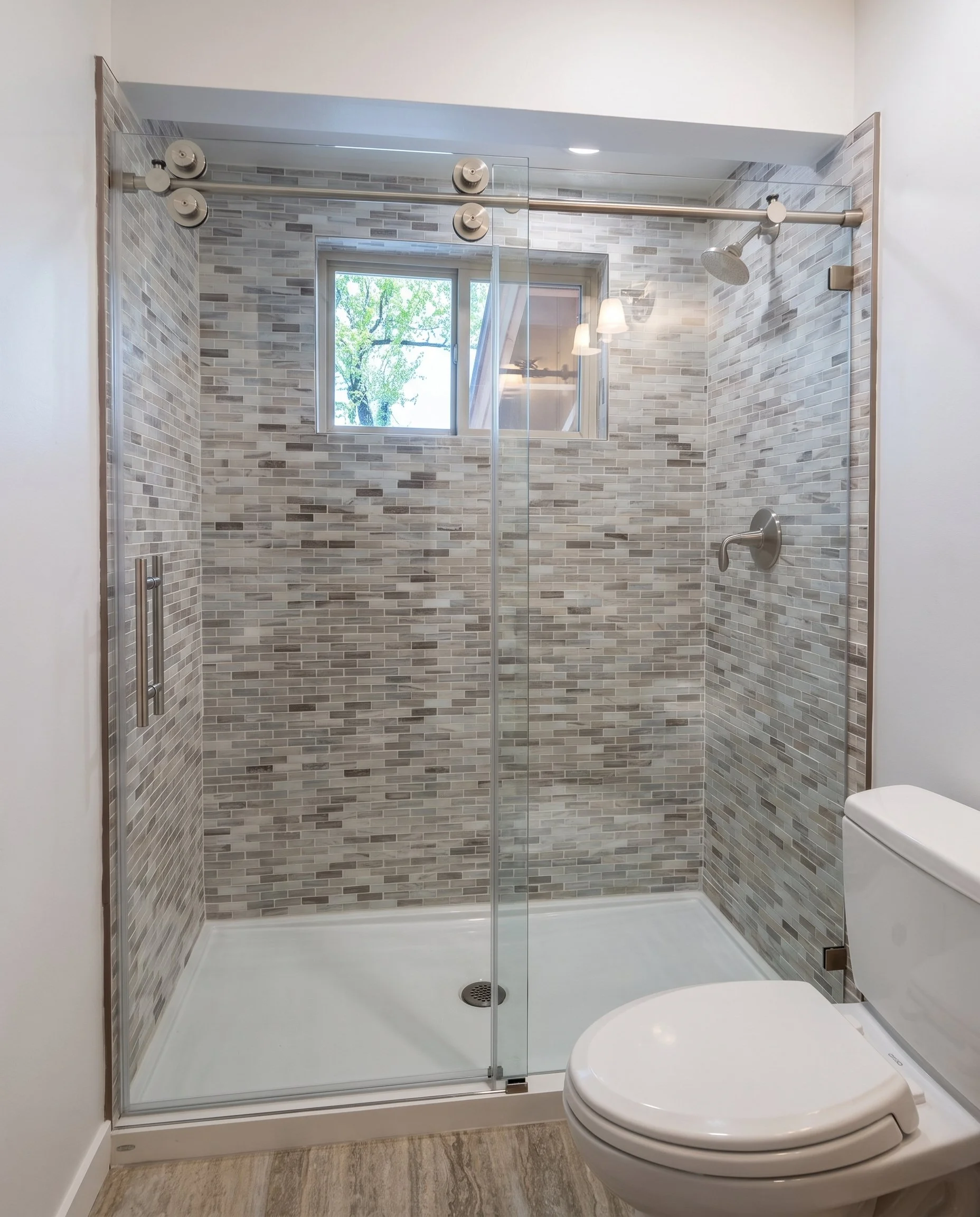 Tiled walk-in shower with a sliding glass door and a window tiled into the surround.