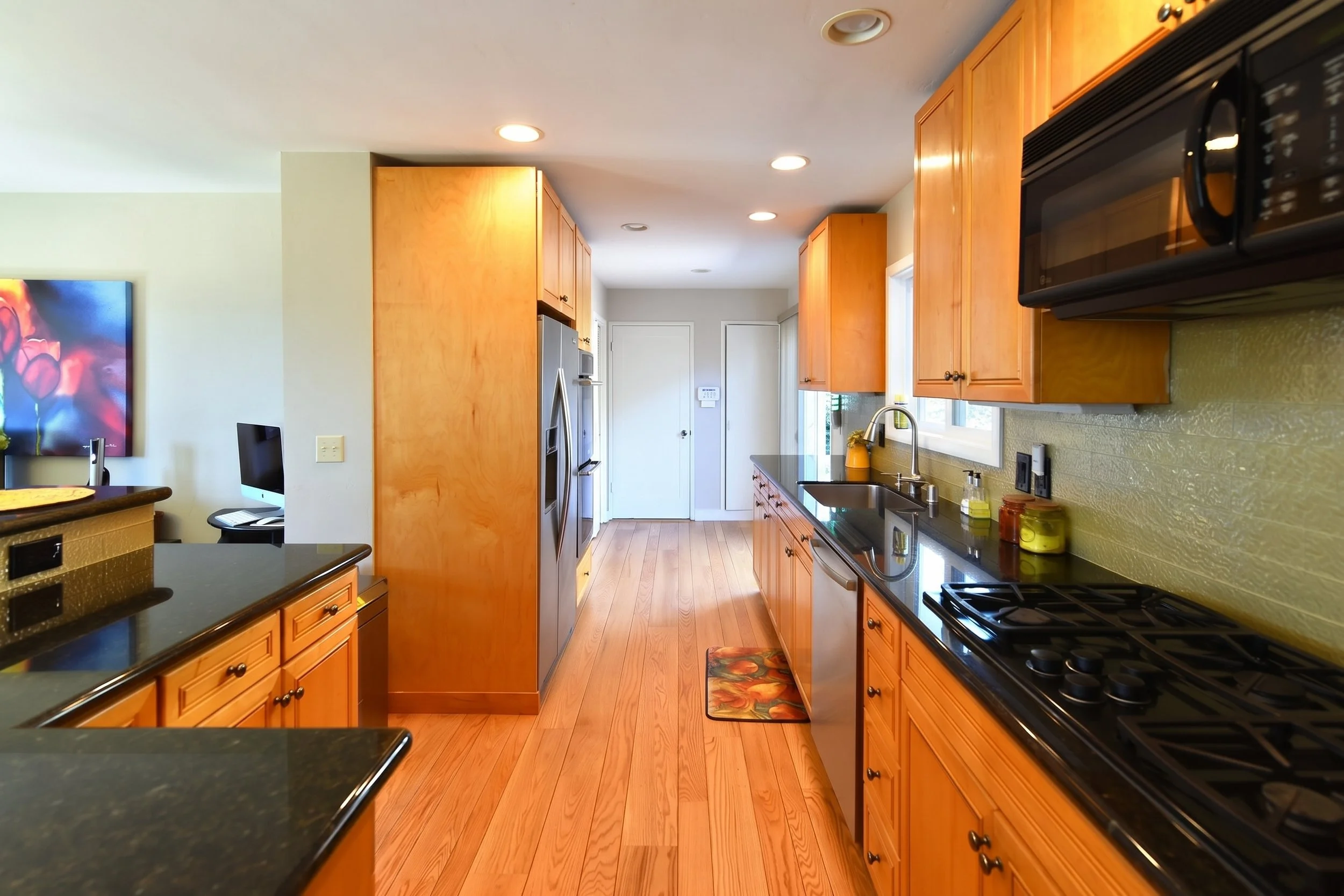 Galley view of the kitchen with maple cabinets and dark stone counters.