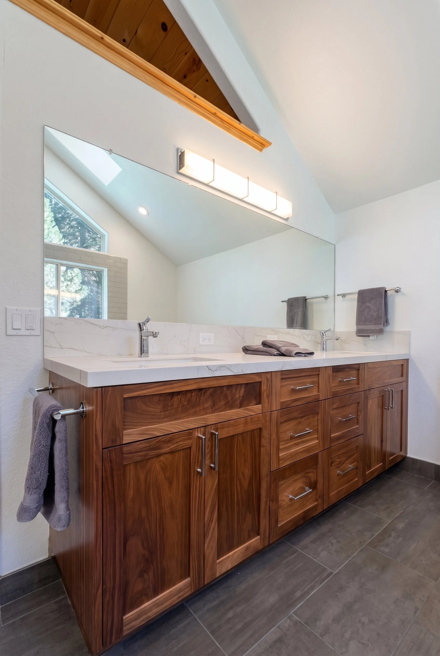Double vanity in dark wood with a stone top, under a vaulted ceiling.