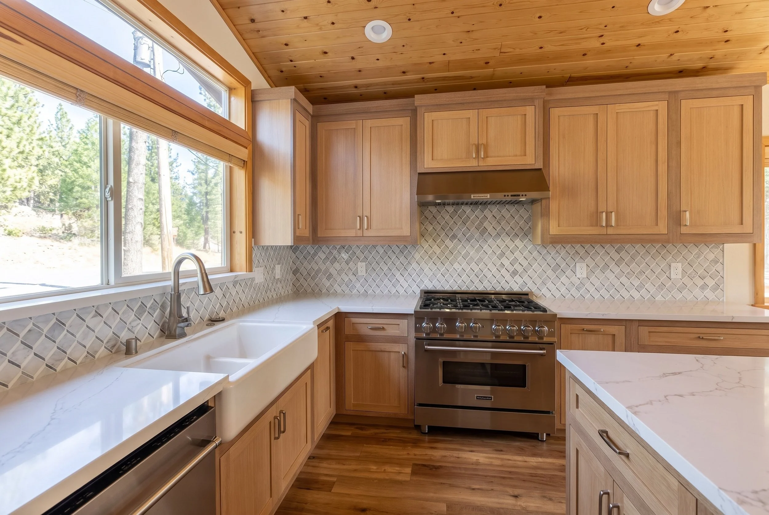 Farmhouse sink under the window, with the range and the white quartz island.