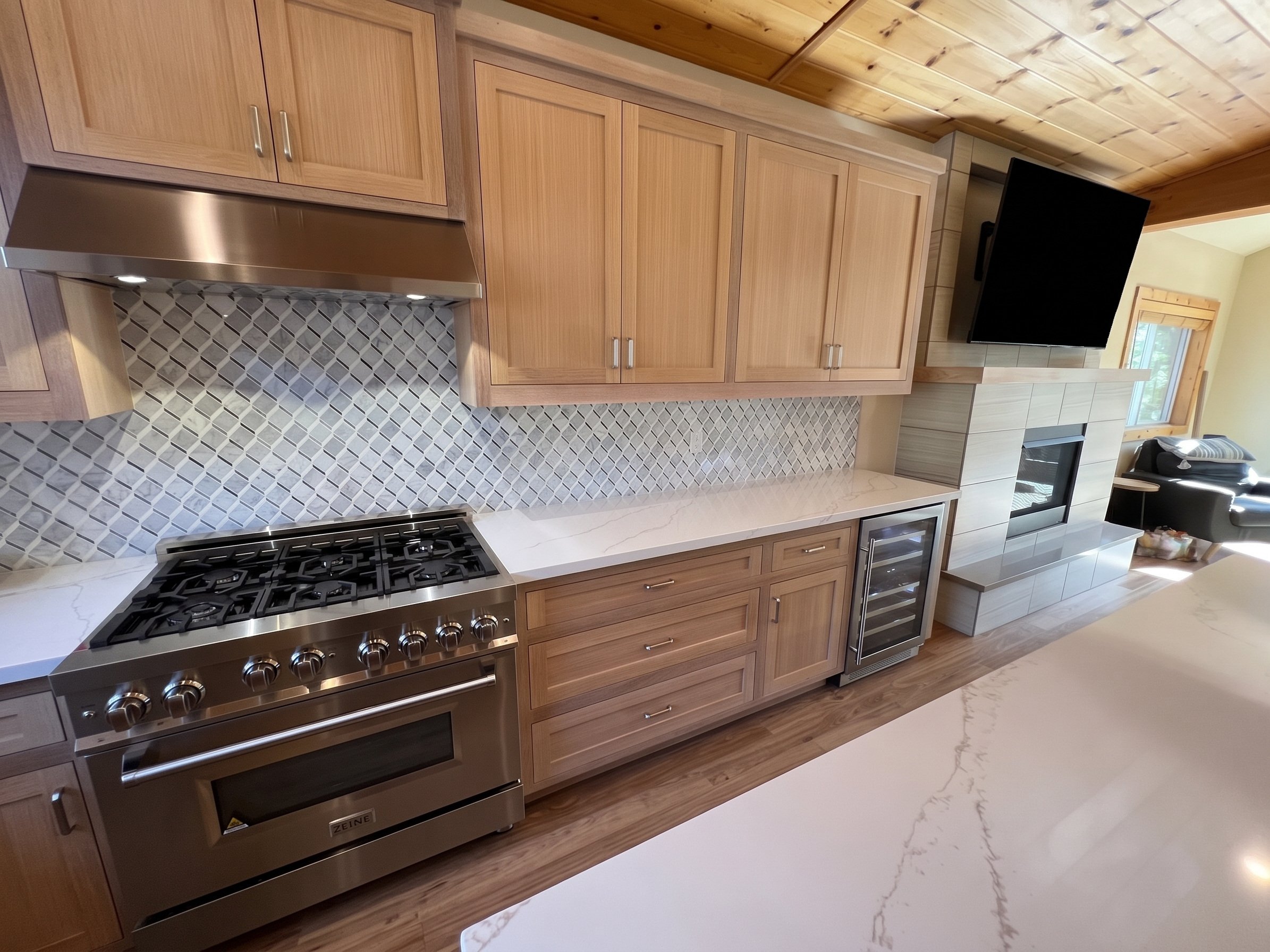 Gas range and stainless hood with the arabesque tile backsplash, seen across the white quartz island.