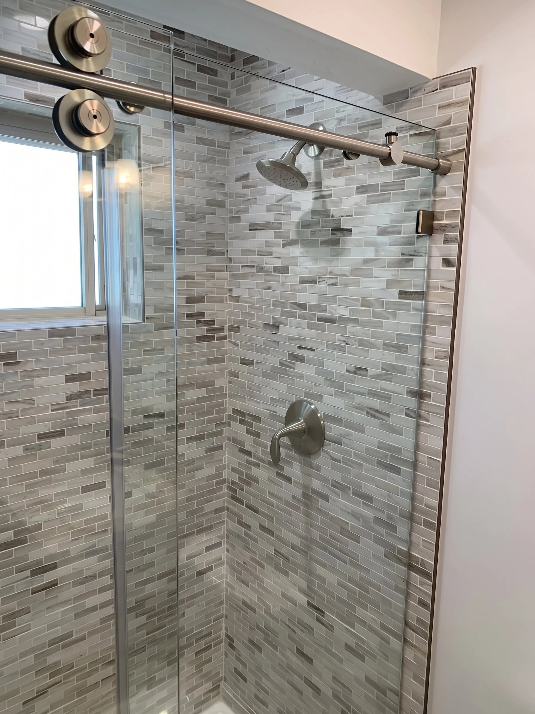 Walk-in shower with gray mosaic tile, a rain head and a sliding glass door.