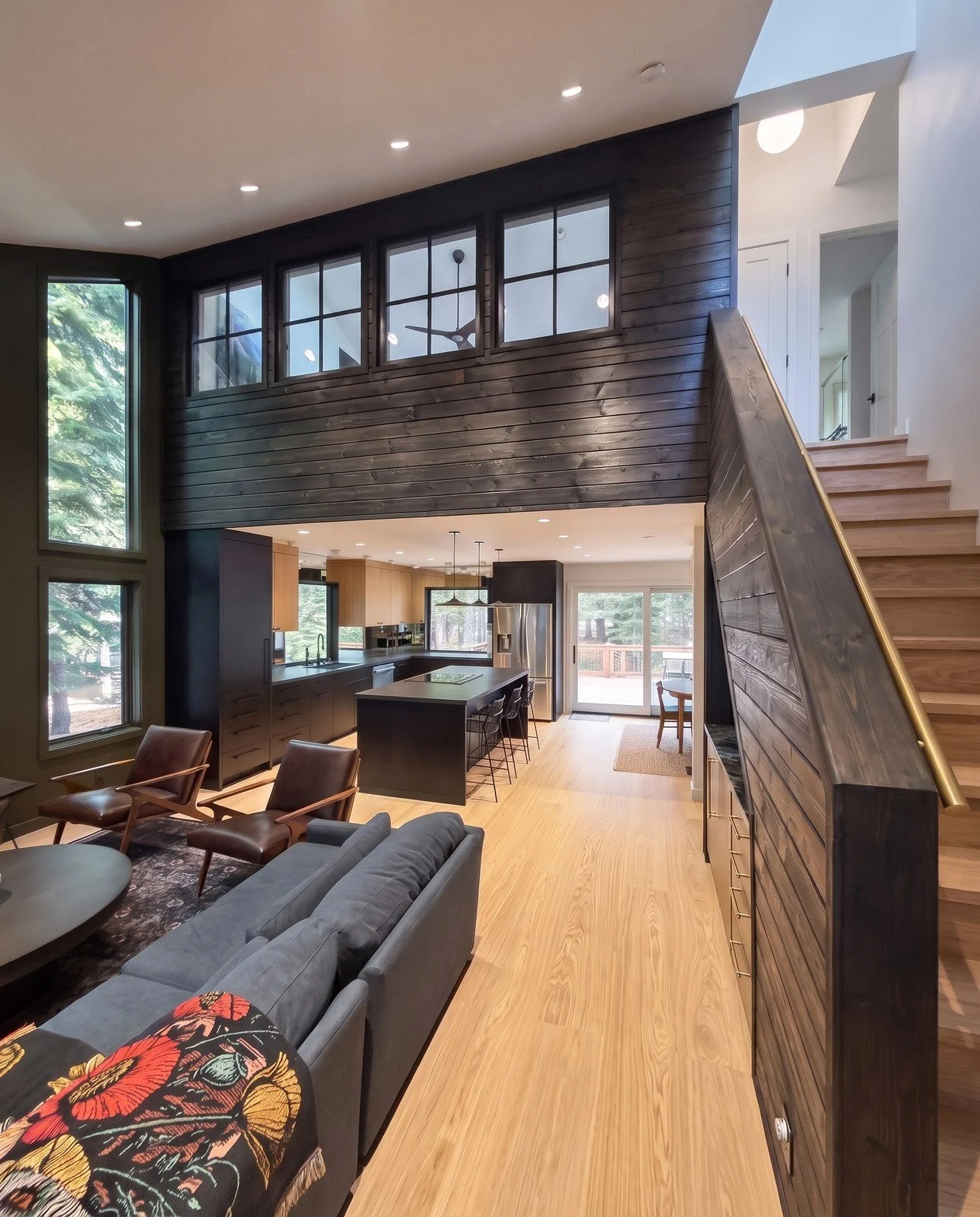 View from a great room toward a black and oak kitchen, under a dark plank wall with four interior windows.