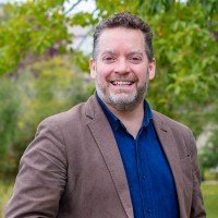A headshot of James Stauch, an executive director of Institute for Community Prosperity, showing him in a bright smile and an outfit of blue shirt and grey vest.