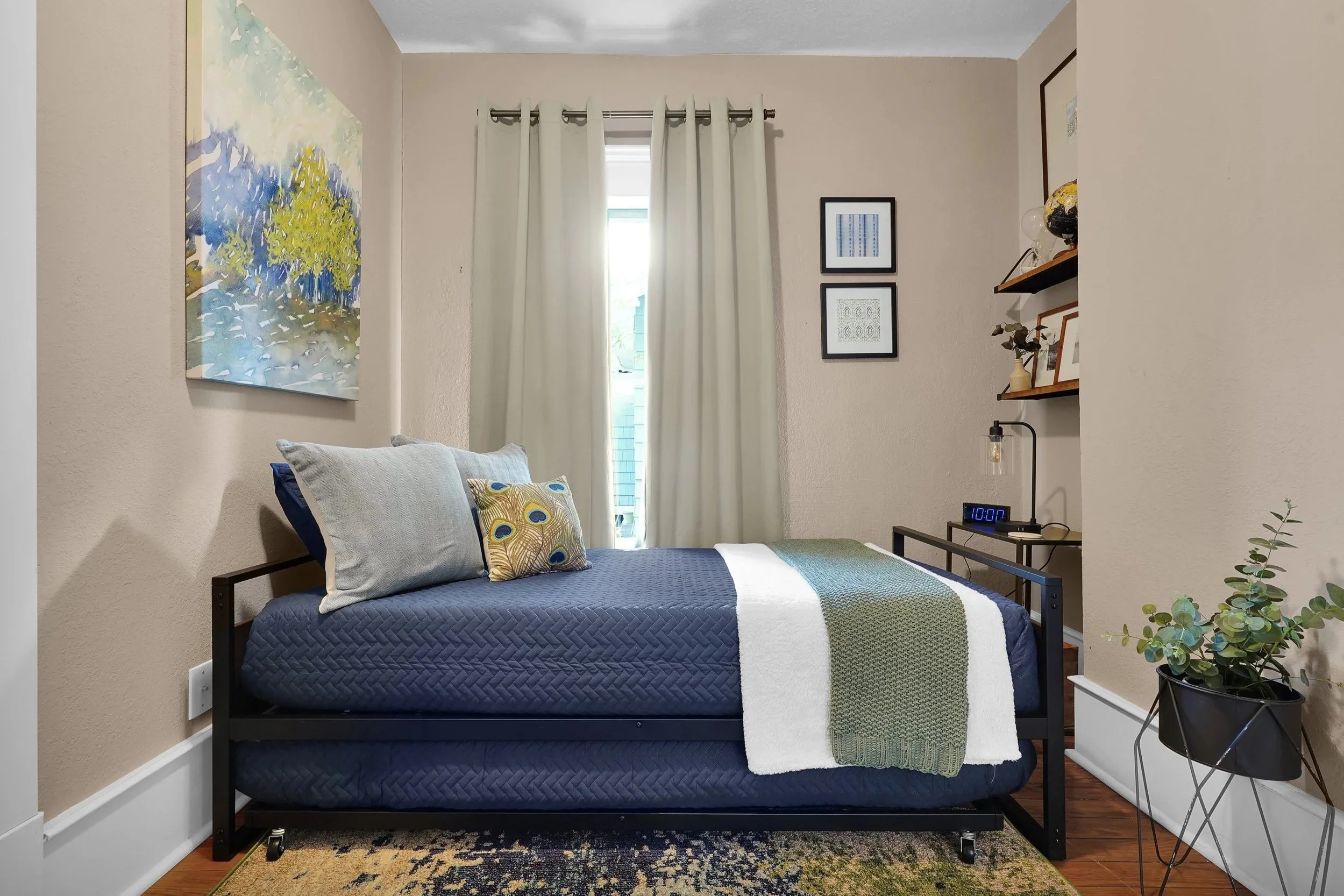 Cozy guest bedroom featuring a black metal daybed with a trundle, dressed in navy blue quilted bedding, light blue pillows, and a peacock feather accent pillow.