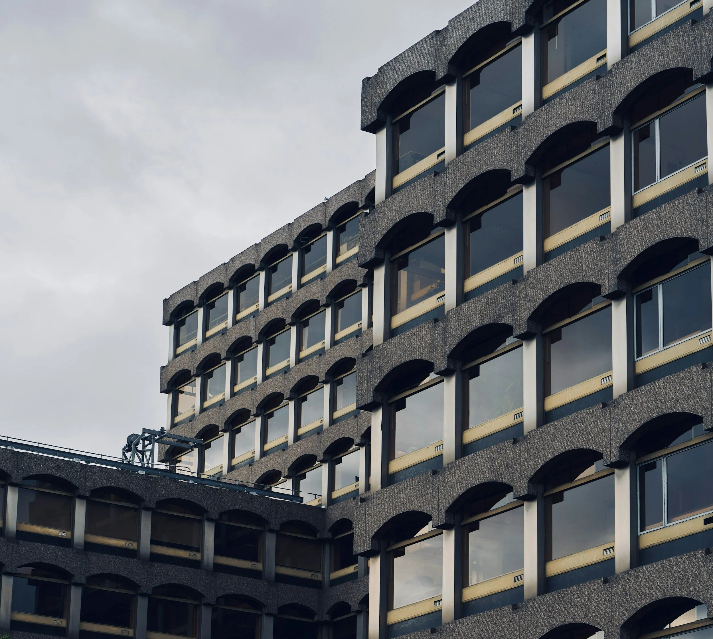 Close-up of a modern multi-story building with multiple windows and arched architectural details on a cloudy sky