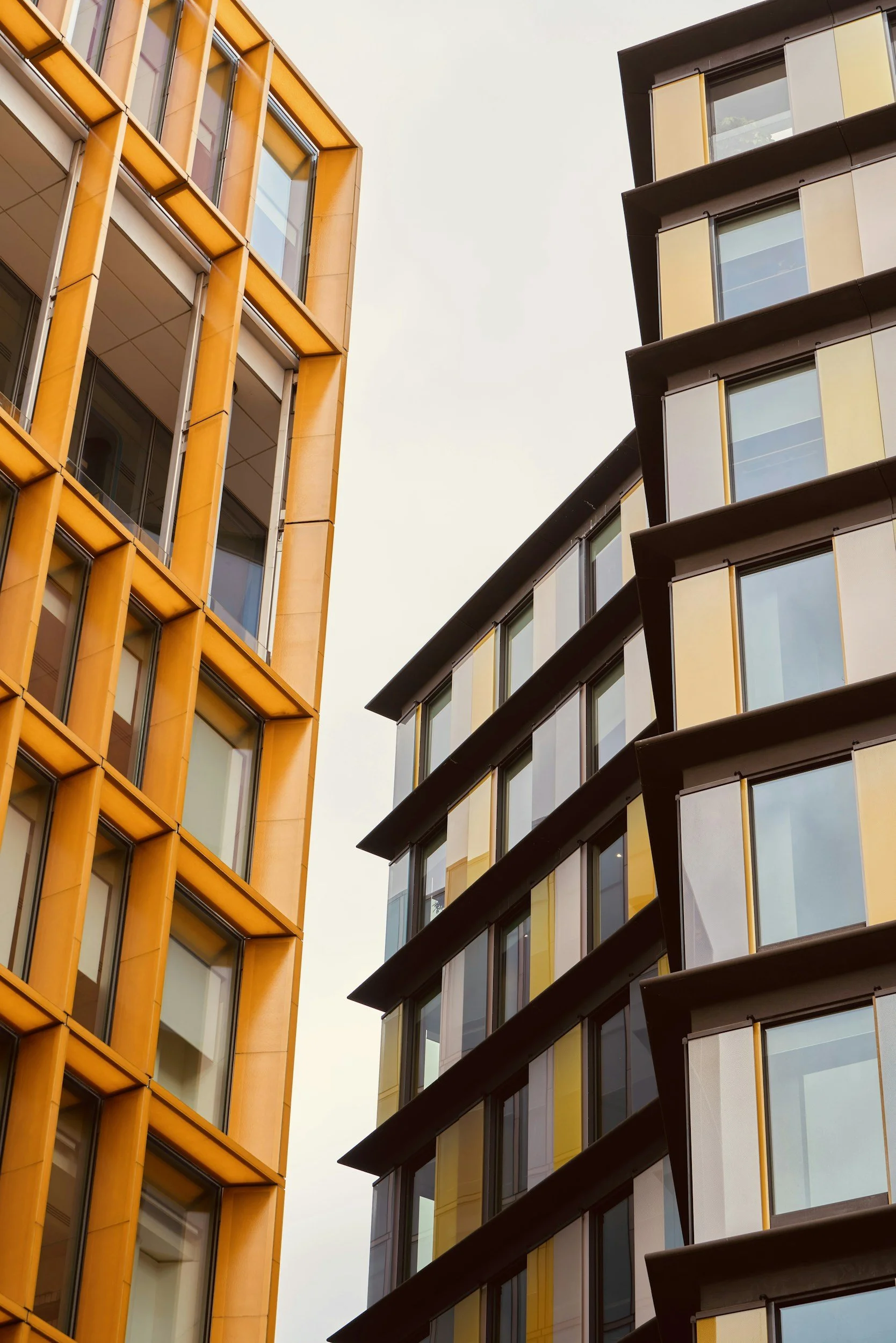 Close-up view of modern apartment buildings with large windows, one building has an orange facade and the other has a dark facade with yellow accents.