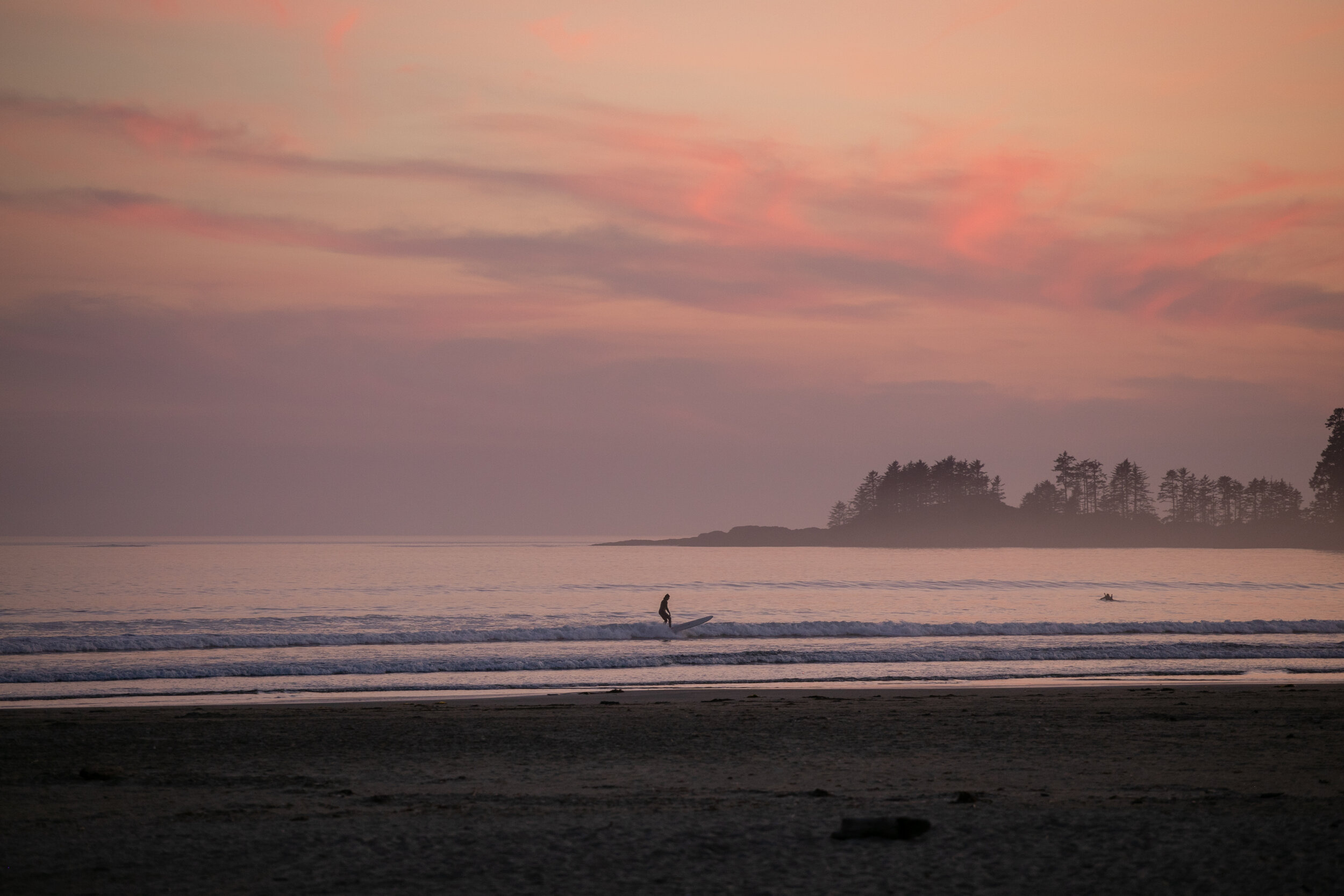 Person surfing at sunset with pink skies in Tofino