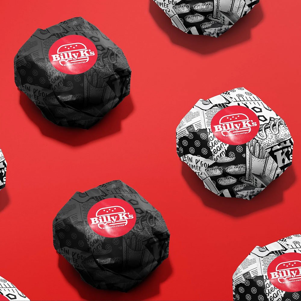 Wrapped burgers from Billy K's on a red surface, with black and white wrapping paper featuring various illustrations and the Billy K's logo.