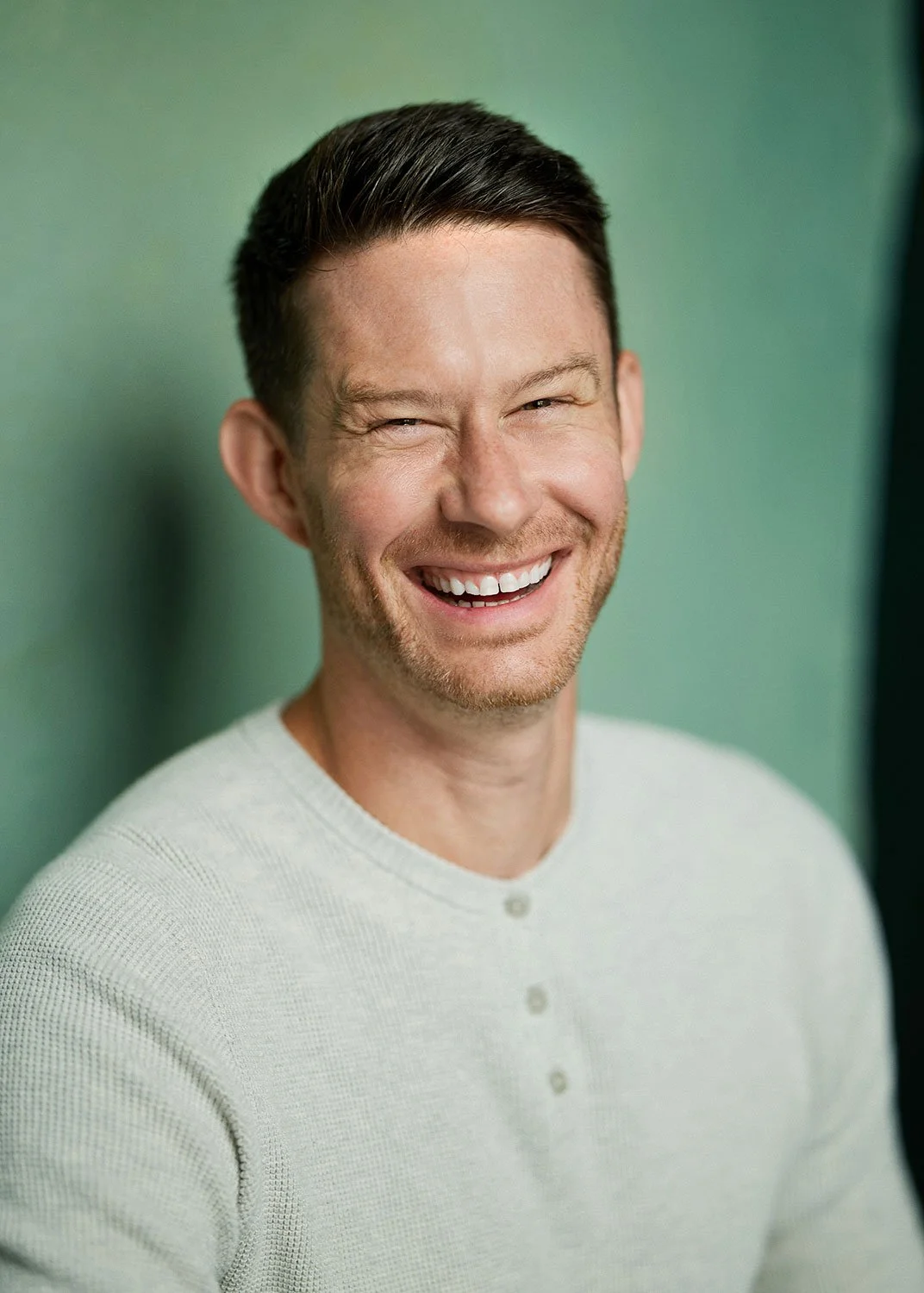 Ryan Labrosse smiling in a white henley against a green background