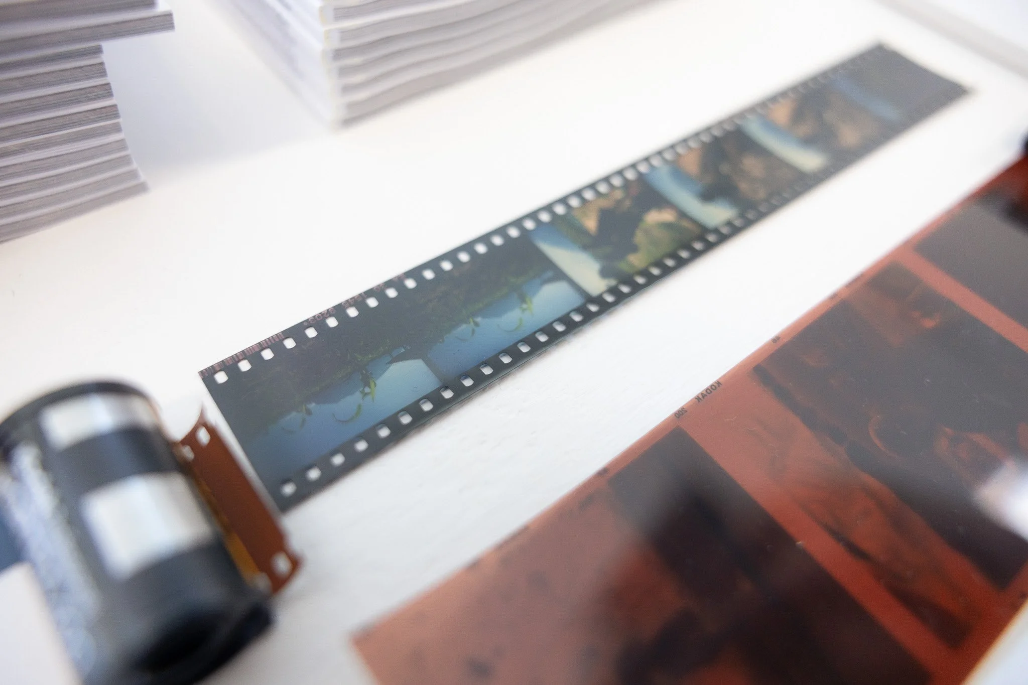 Close-up of a strip of photographic film resting on a white surface with stacks of paper or film nearby.