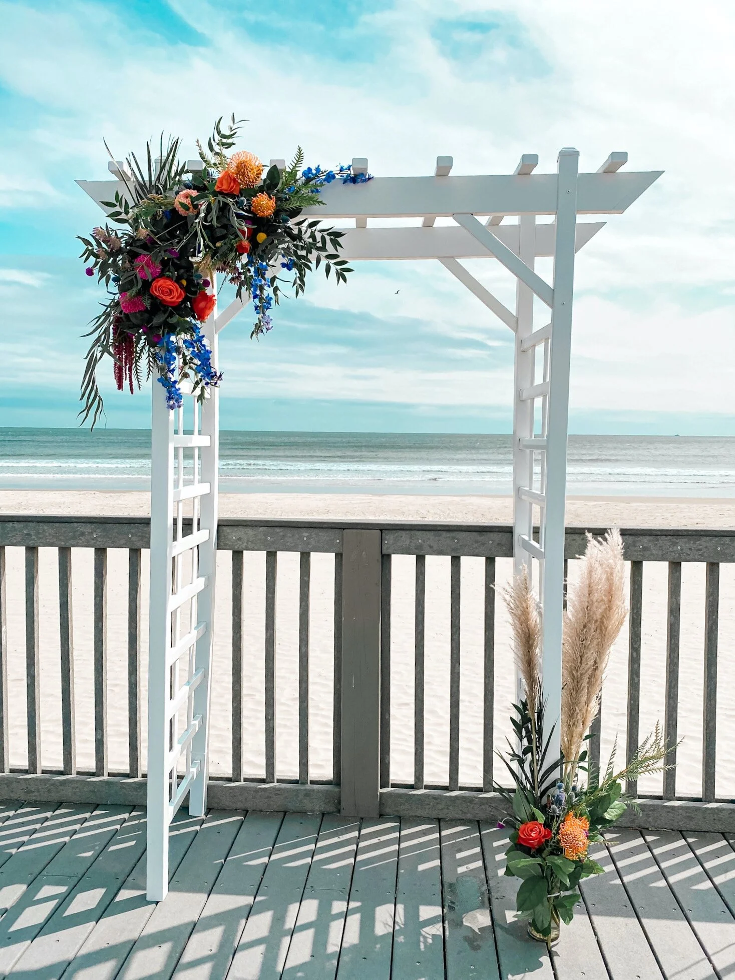 Arbor built to last against the wind while giving a destination wedding feel. Protea, amaranthus, and delphinium were featured.