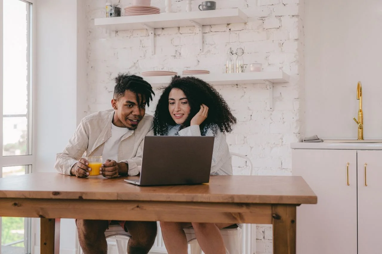 a-couple-sitting-looking-at-a-computer-laptop-on-a-wooden-table